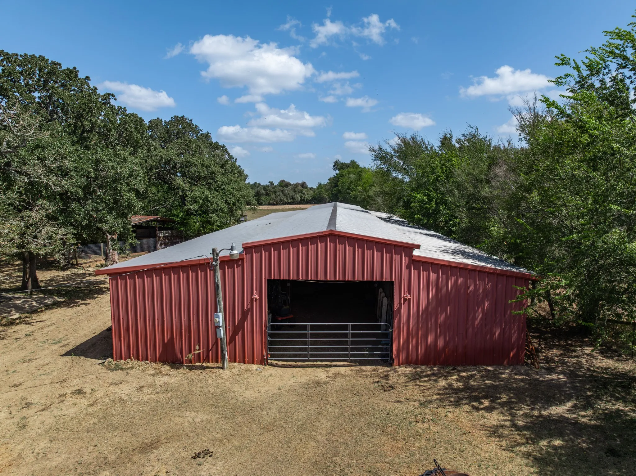 Red metal-sided barn with a silver roof, featuring a large open entrance and a metal gate