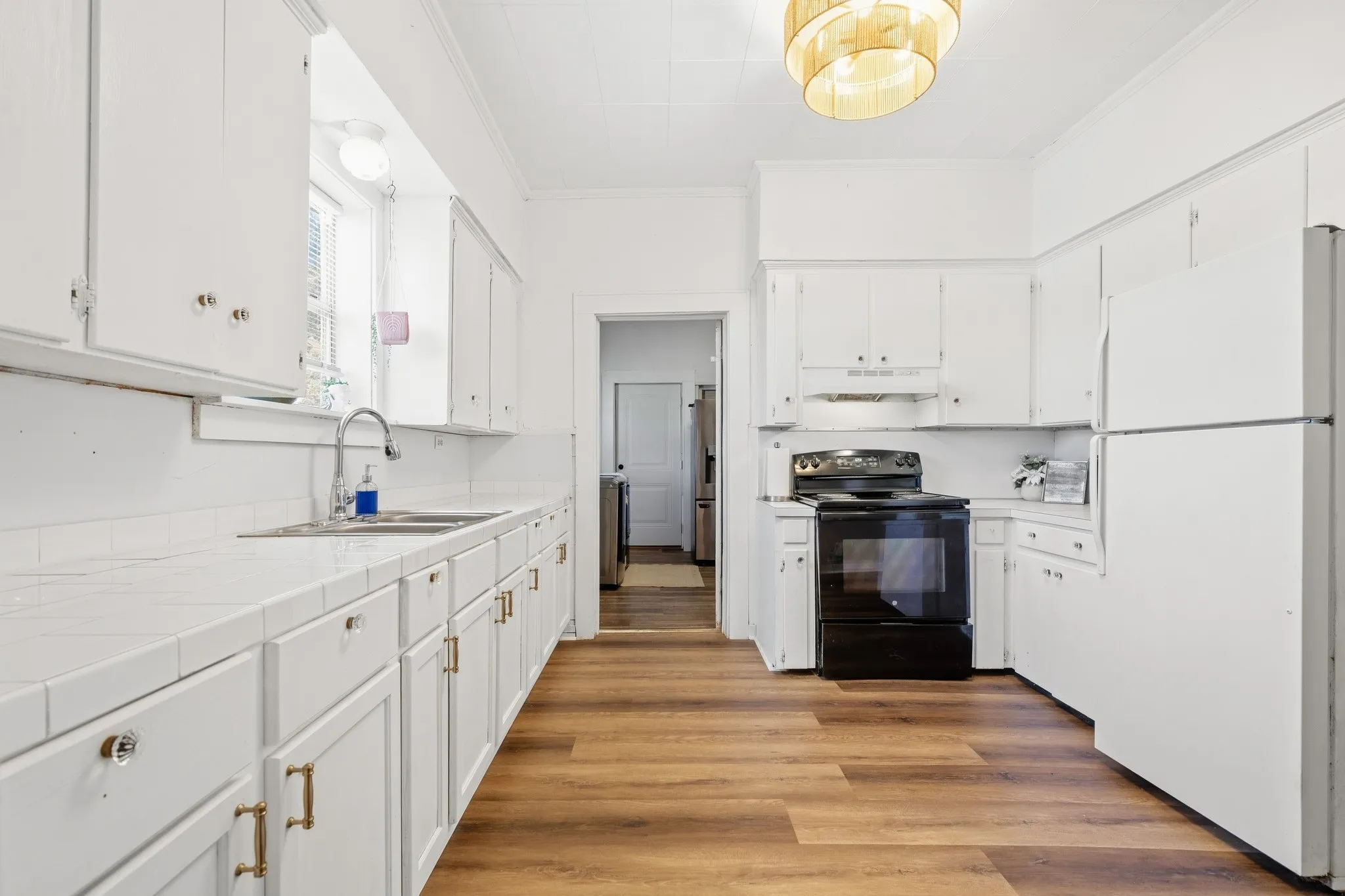 Full kitchen featuring white cabinetry, black appliances, wood-finish flooring, white tile countertops, and a ceiling-mounted light fixture