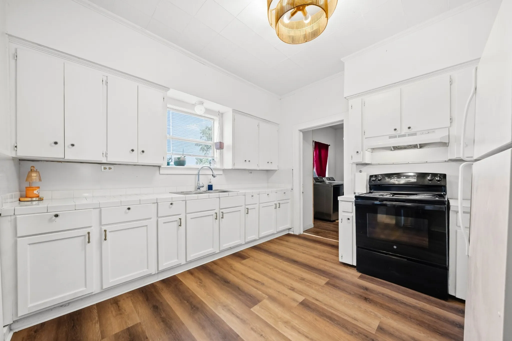 Kitchen featuring wood-finish flooring, white cabinetry, a stainless steel sink, and white tile backsplash