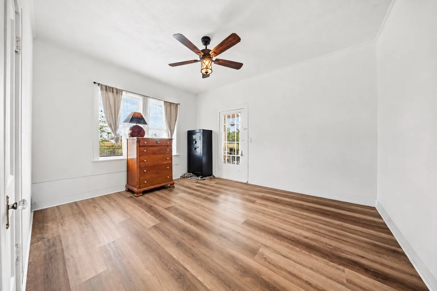 Wood-finish flooring throughout, bright white walls, multiple window openings, and a ceiling fan with integrated lighting