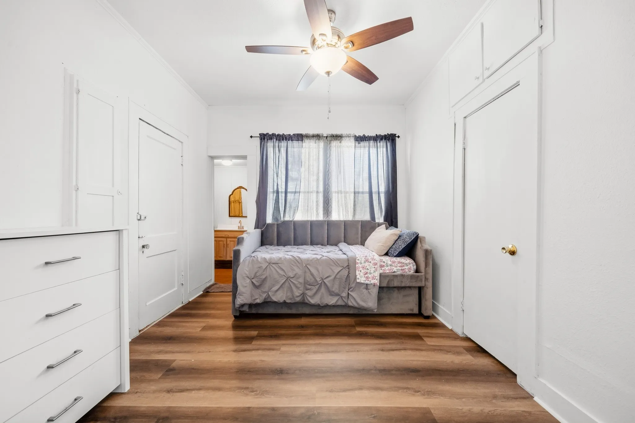 Wood-finish flooring, ceiling fan with light fixture, window with drapery, and built-in closet with upper cabinetry