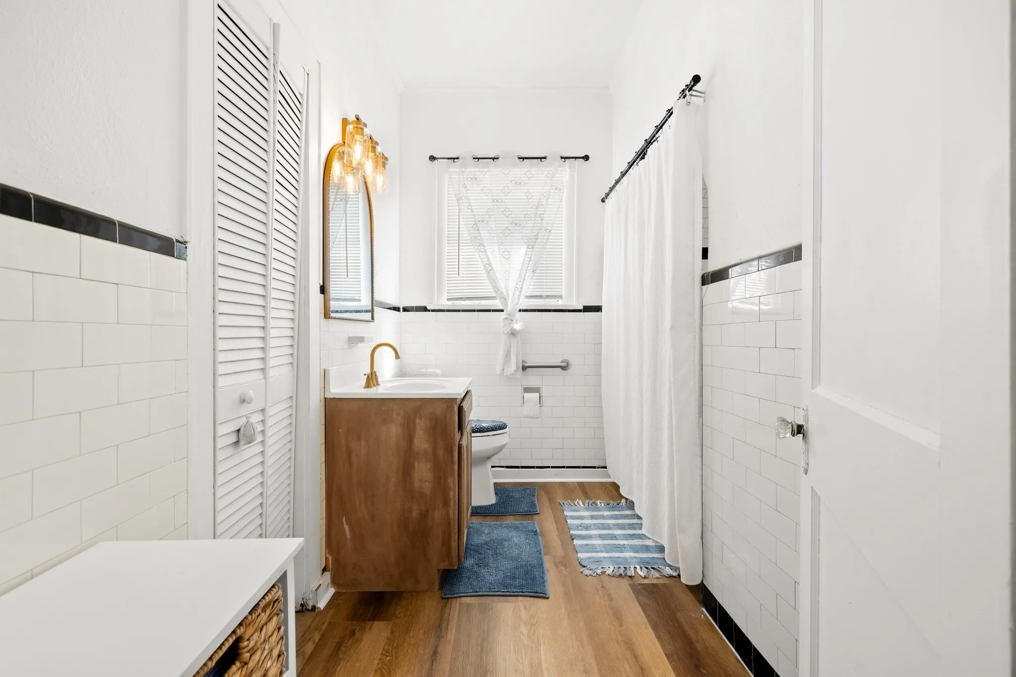 Wood-finish flooring with white subway tile walls and black accent trim