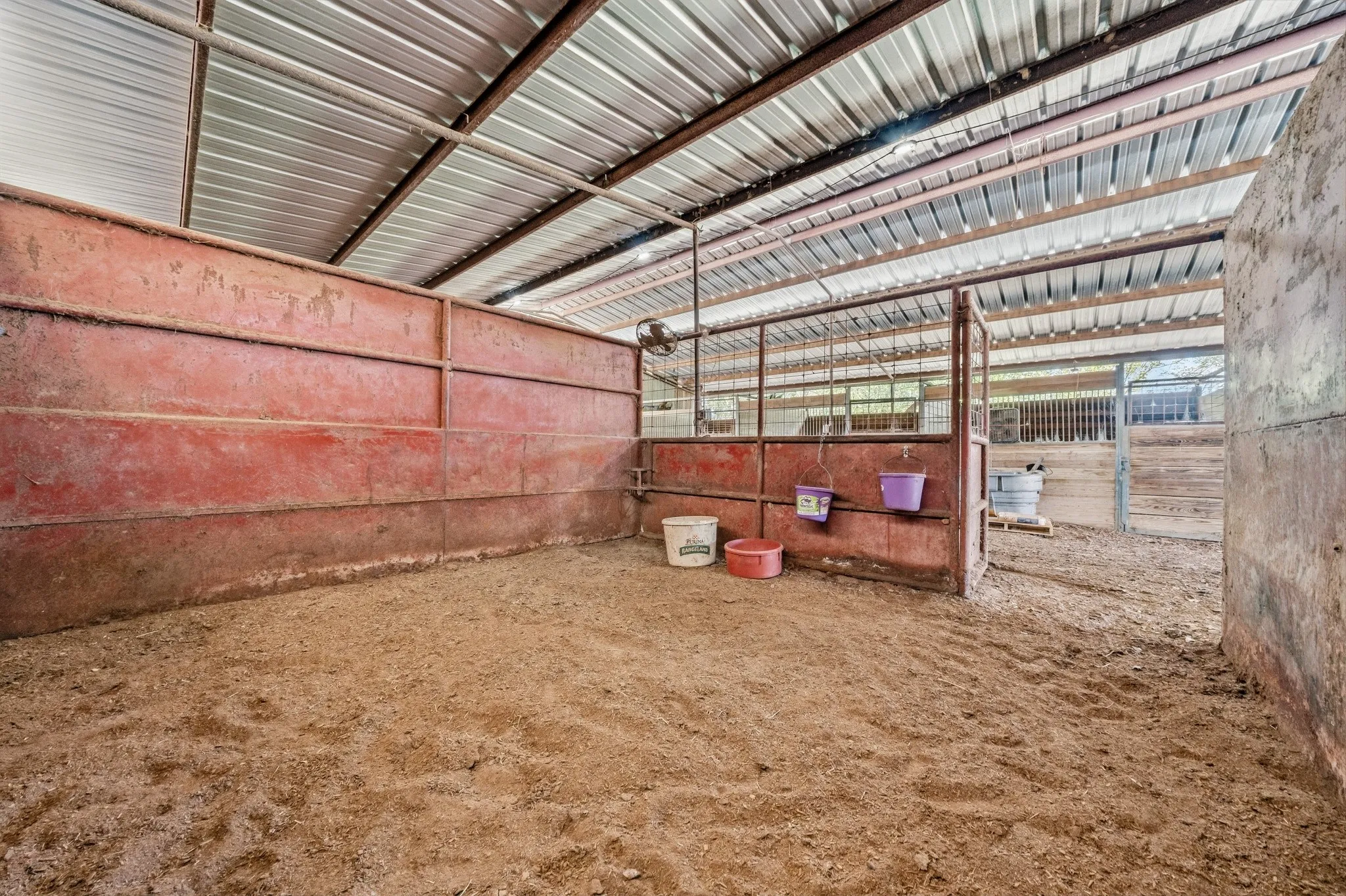 Open-air barn stall with a metal roof, metal framing, and a dirt floor