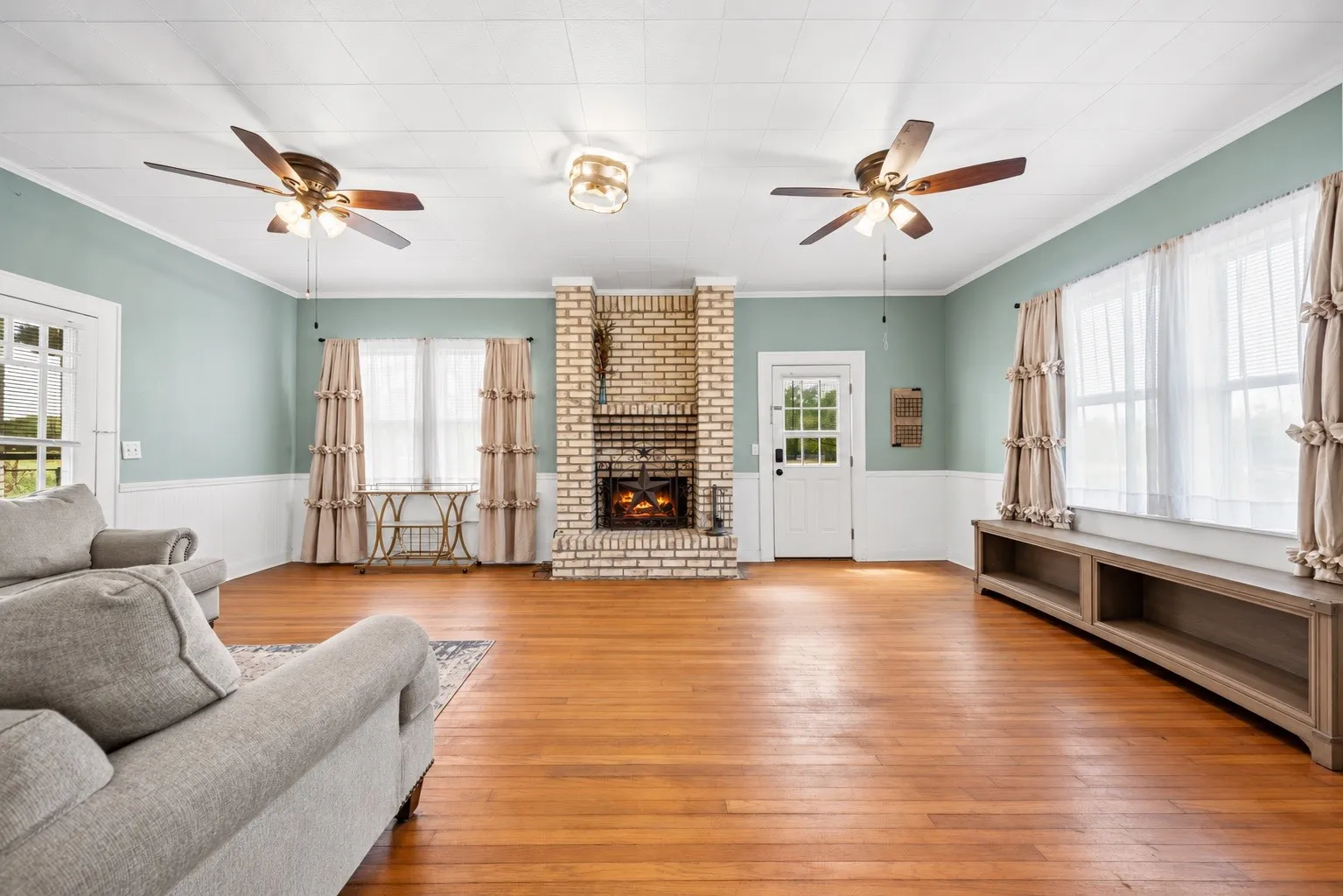 Hardwood flooring, brick fireplace, transom windows, wainscoting, and ceiling fans