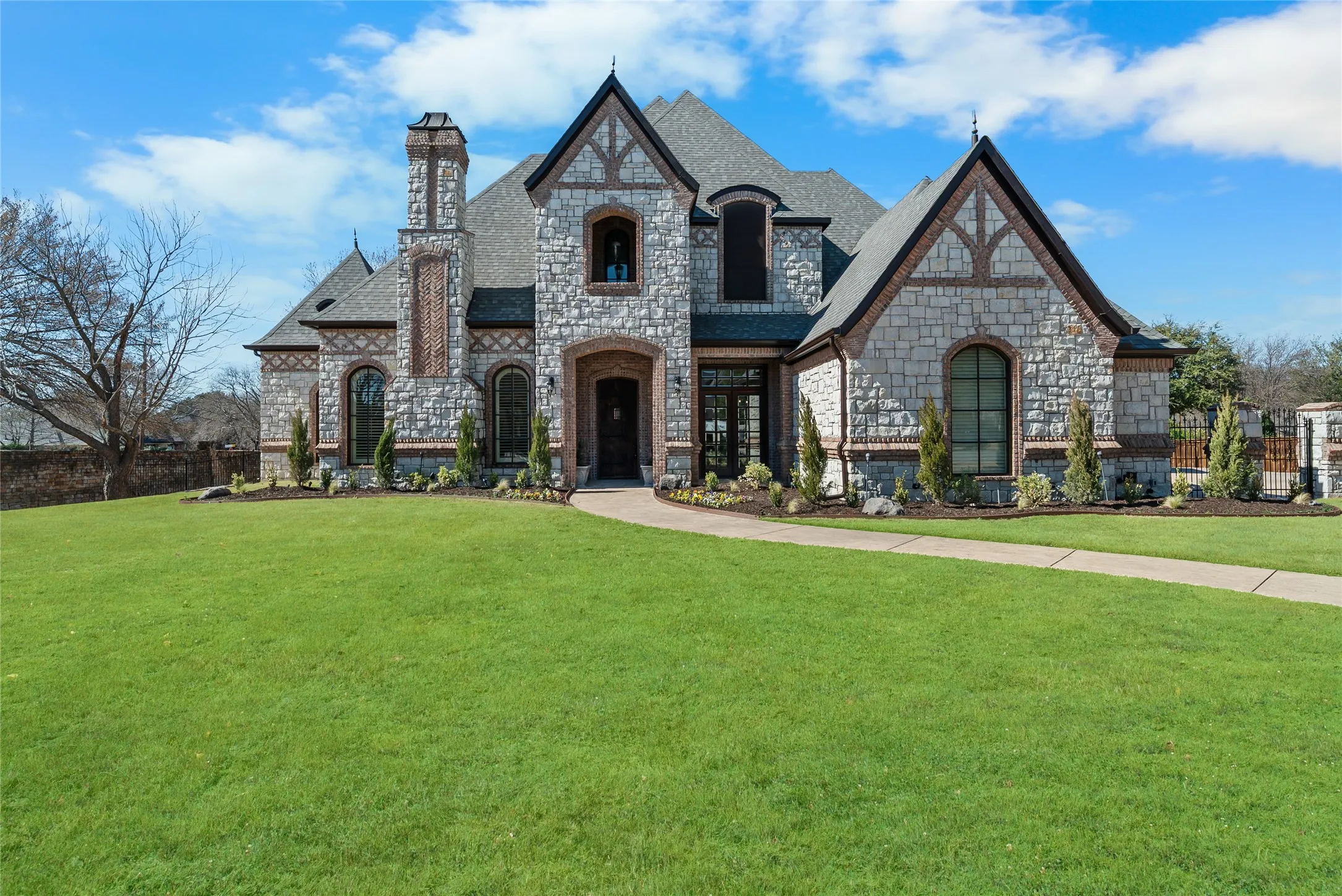 Stone and brick exterior with arched windows, prominent chimney, and a landscaped front yard