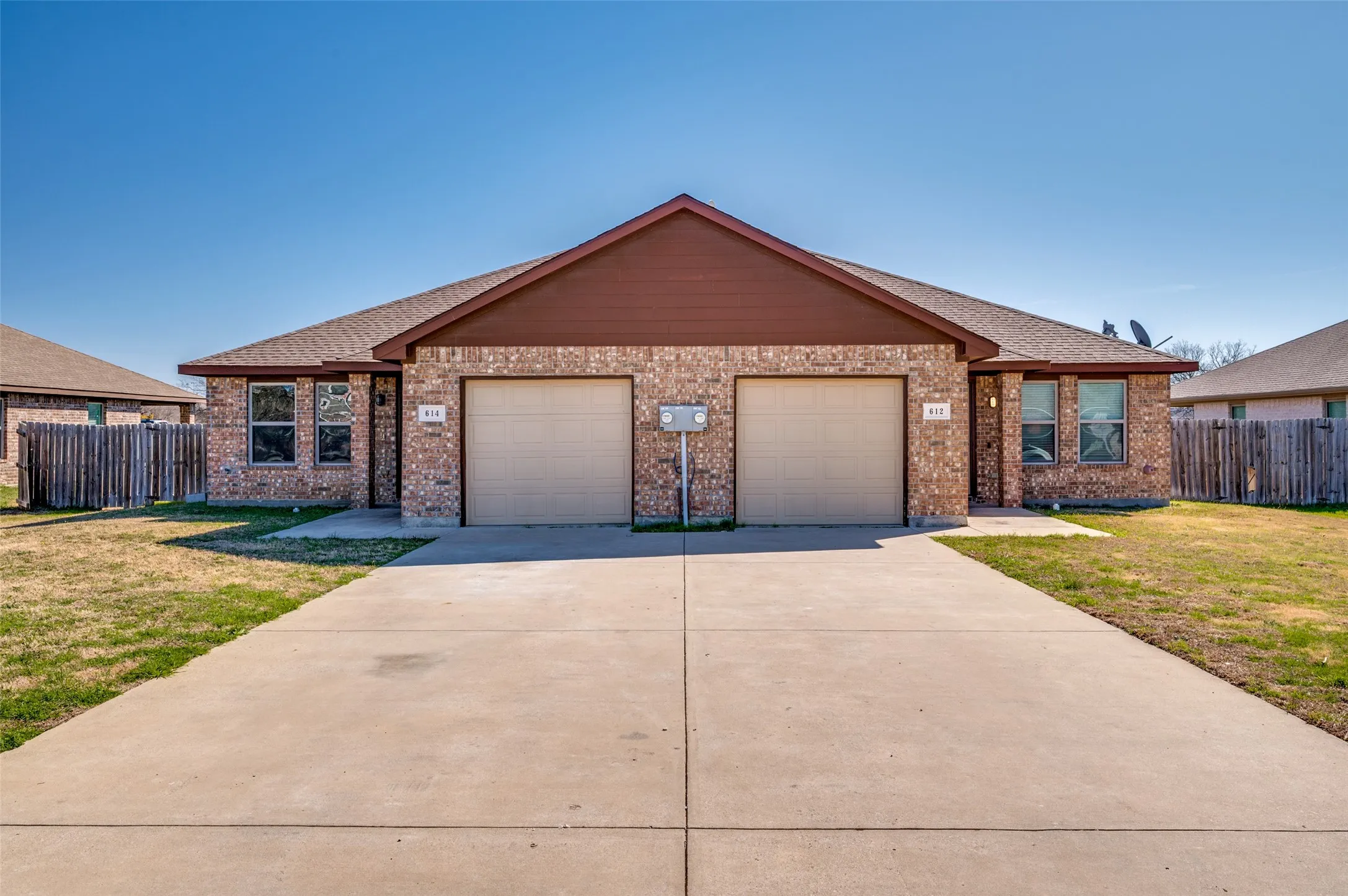 Brick exterior with brown siding, two single-car garages, and a concrete driveway