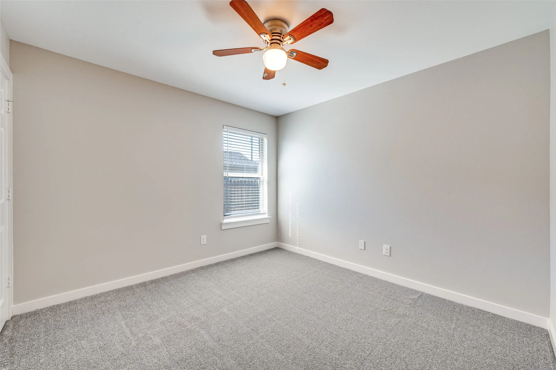 Neutral wall color, window with blinds, overhead ceiling fan with light, and gray carpet flooring