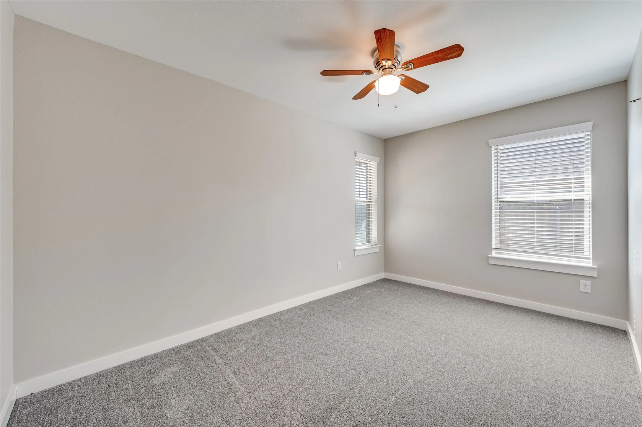Neutral wall paint, plush carpeting, ceiling fan with wood-finish blades, and two windows with blinds