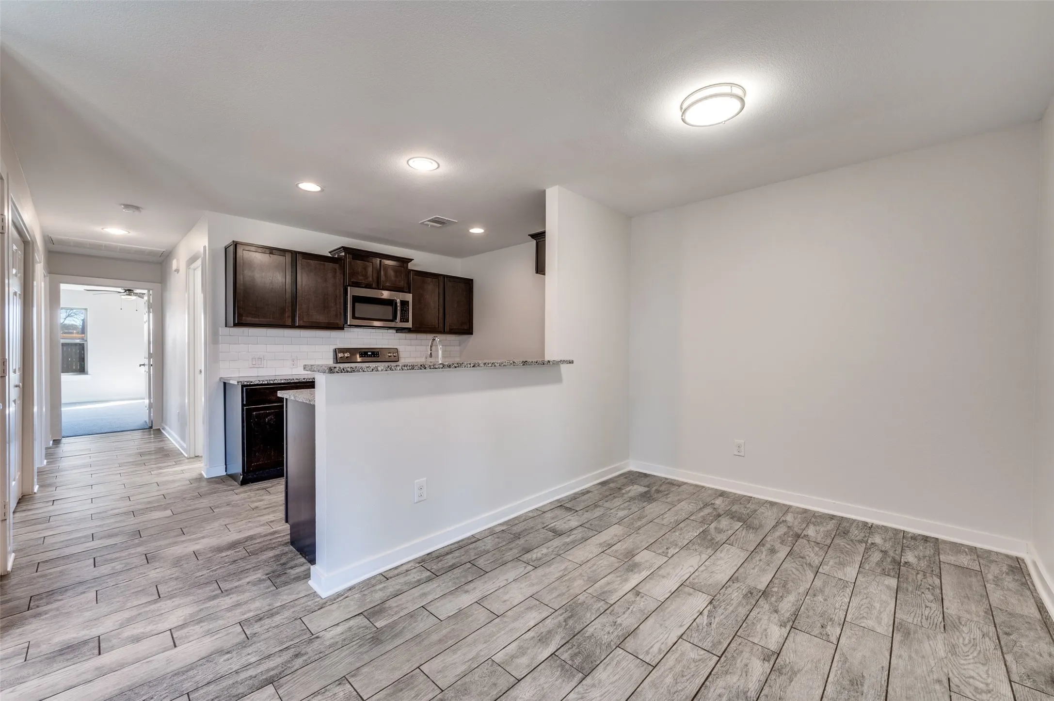 Wood-finish flooring throughout, kitchen with dark wood cabinetry, stainless steel microwave, and white subway tile backsplash