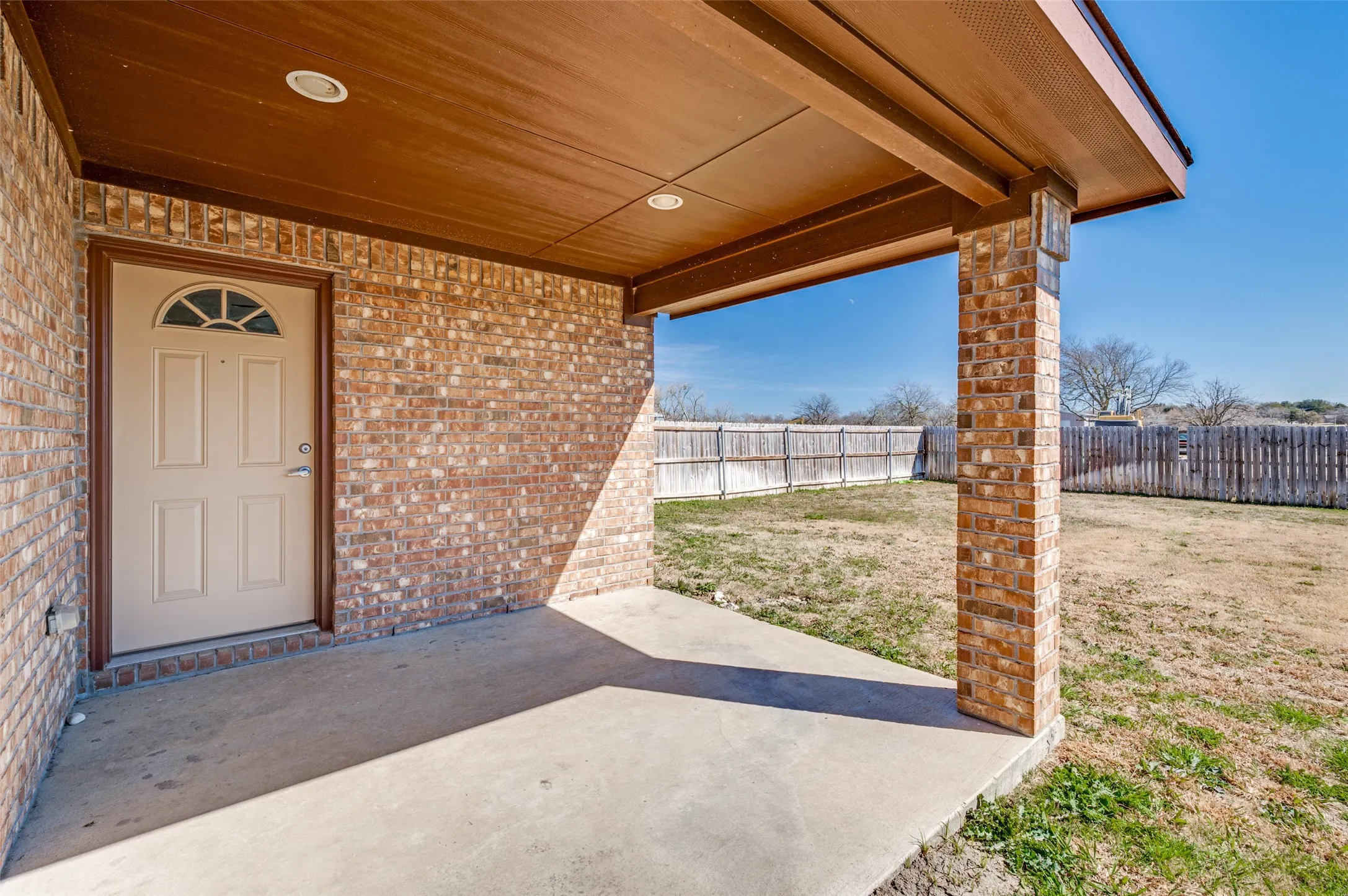 Covered concrete patio with recessed lighting, brick exterior, and a paneled entry door with an arched transom