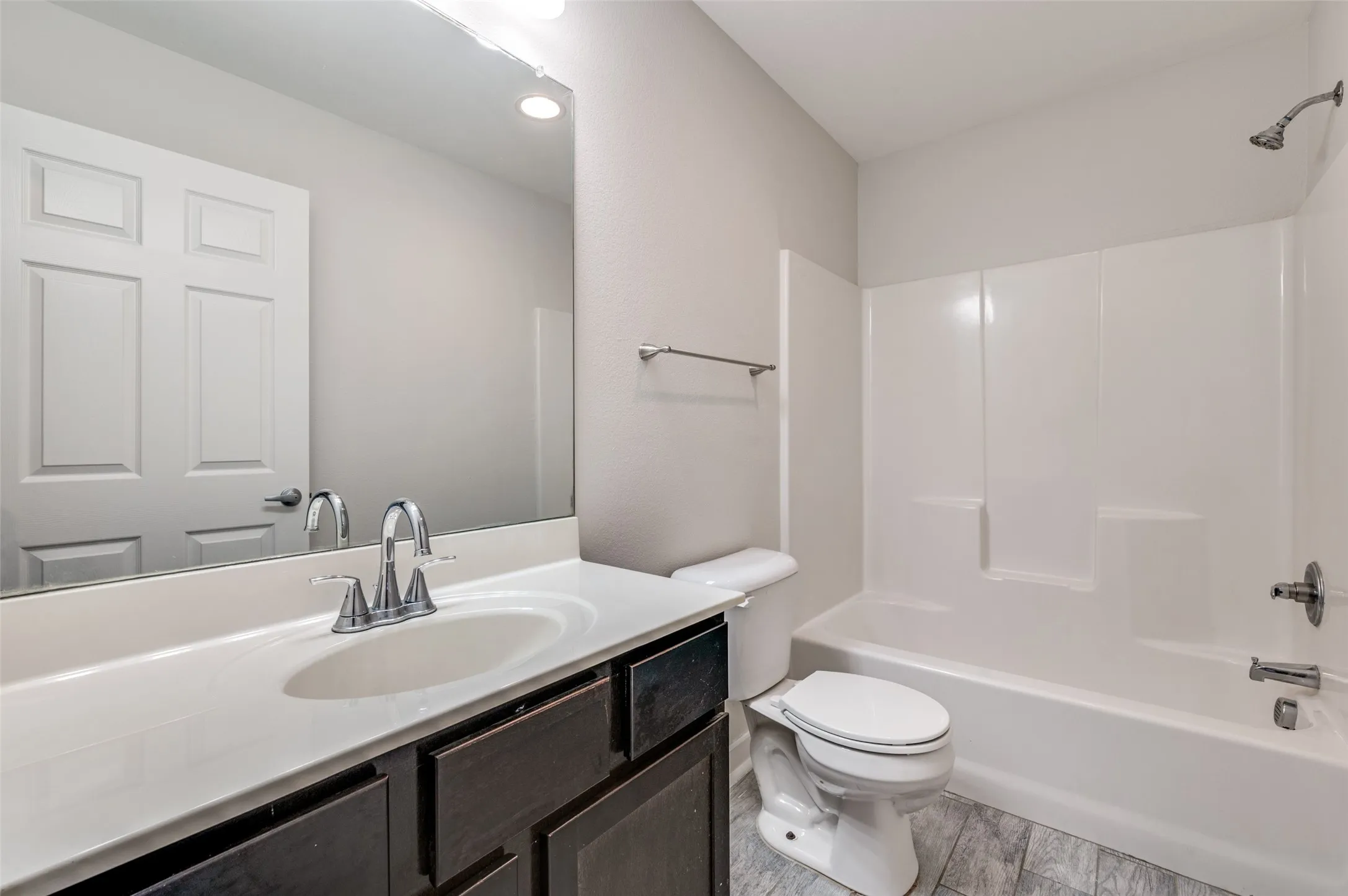 Bathroom featuring a vanity with dark wood-finish cabinetry, an integrated sink, a large wall mirror, and a shower-tub combination with a white surround