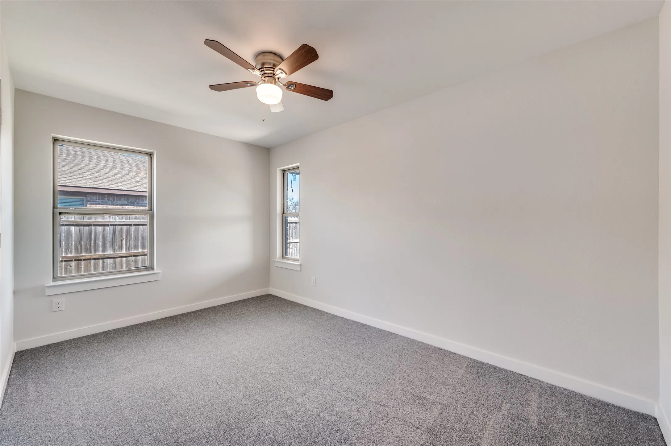 Neutral wall paint, gray carpet flooring, ceiling fan with integrated lighting, and two windows