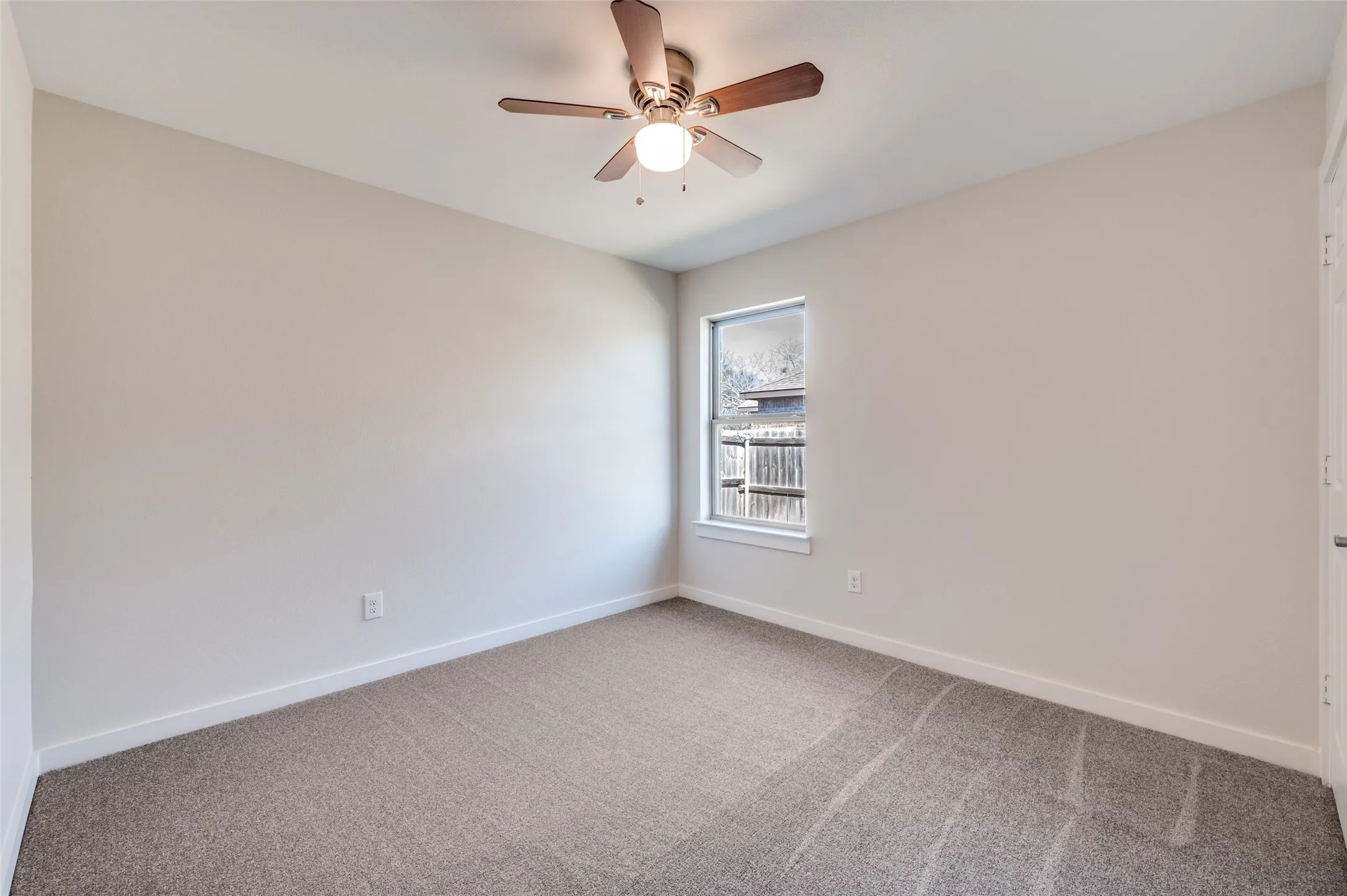 Neutral wall tones, gray carpeting, single window, and a ceiling fan with light fixture