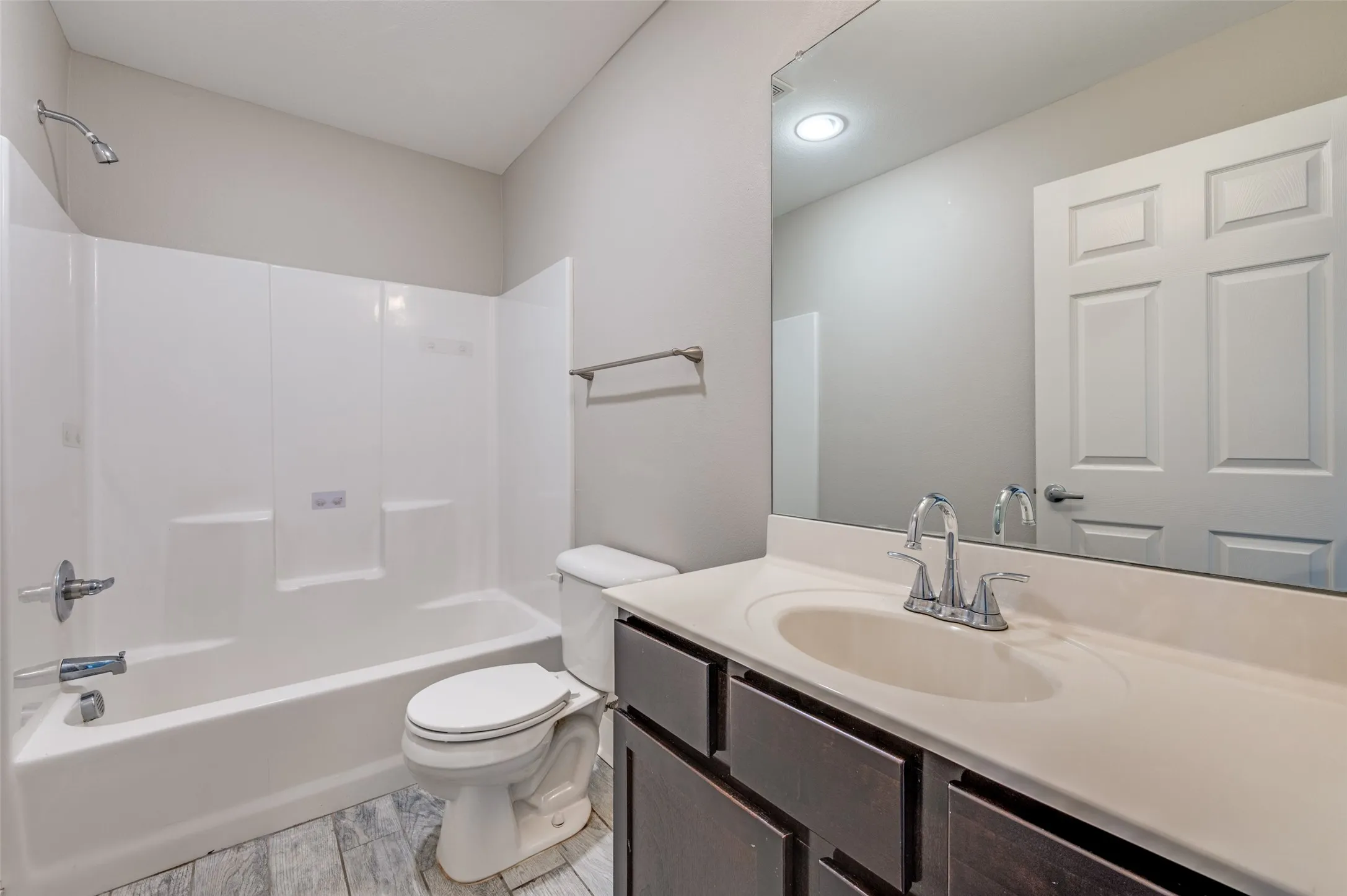 Full bathroom featuring a single vanity with an integrated sink, a large wall-mounted mirror, wood-finish flooring, and a shower-over-tub combination