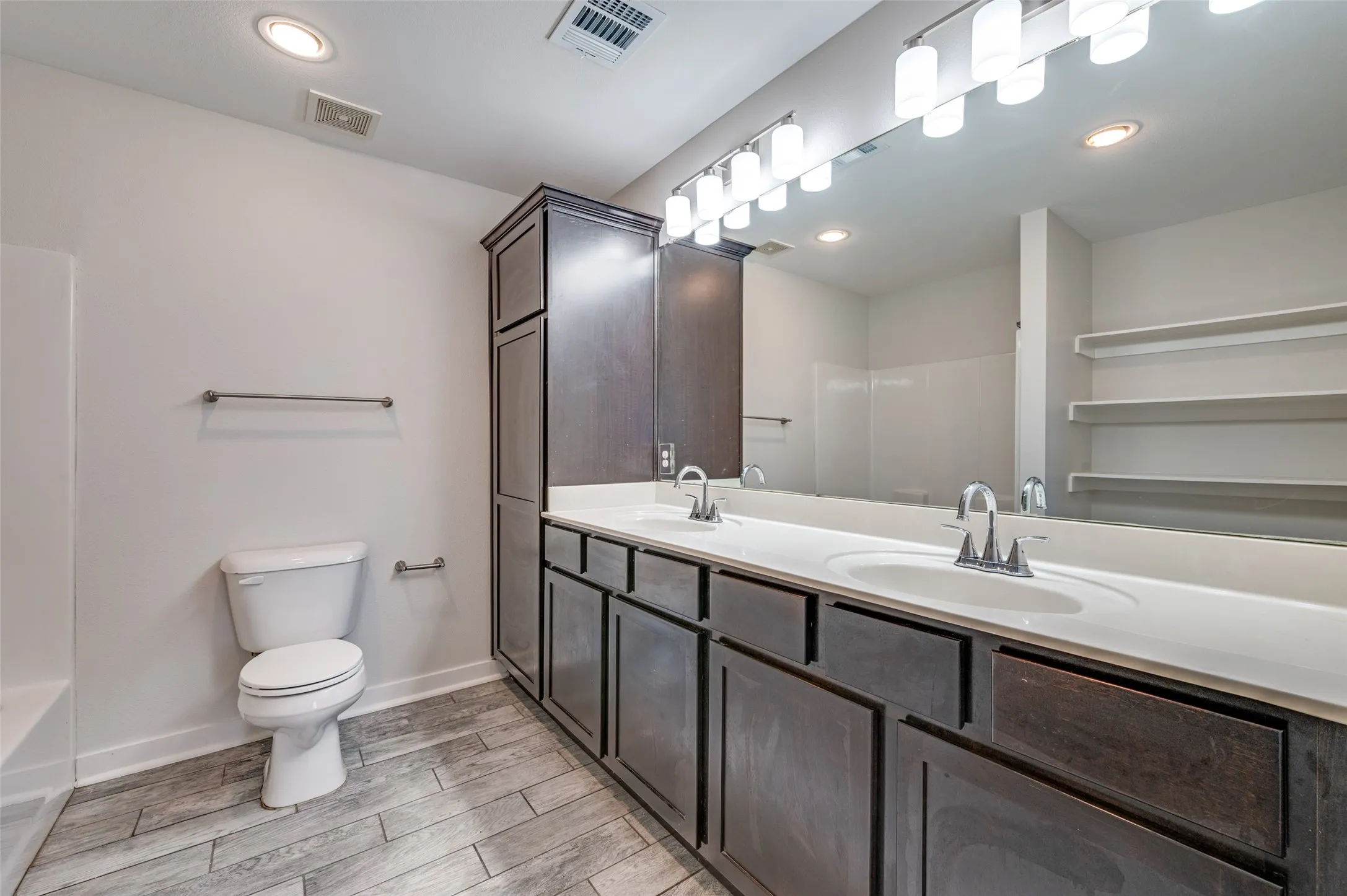 Dual vanity with white undermount sinks, wood-finish cabinetry, and an expansive wall mirror