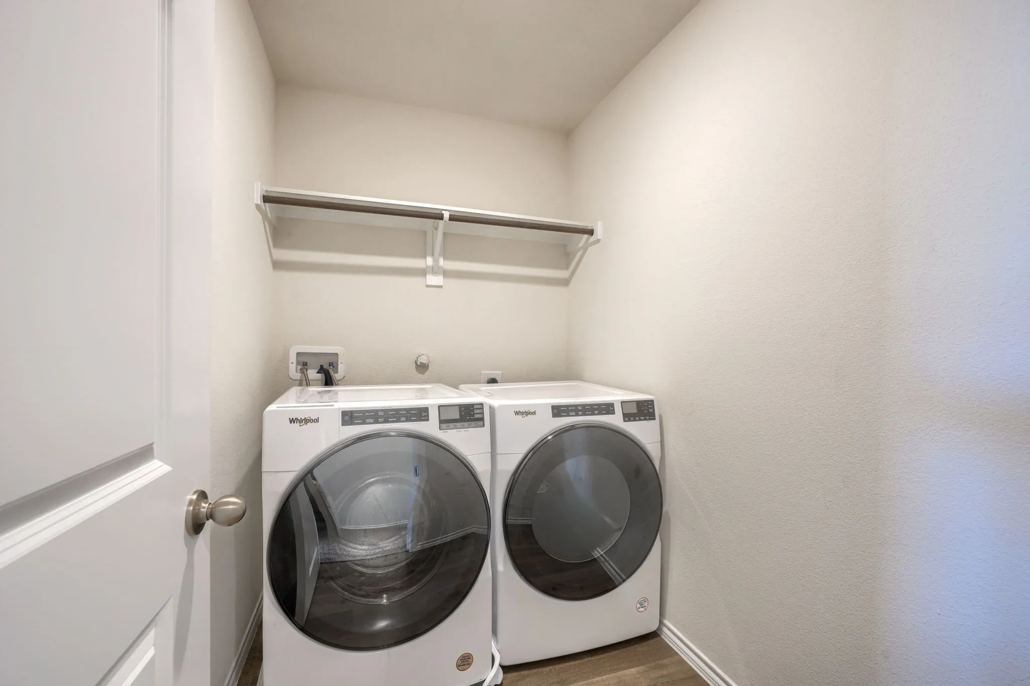 Dedicated laundry area with a built-in hanging rod, wall-mounted utility box, and wood-finish flooring