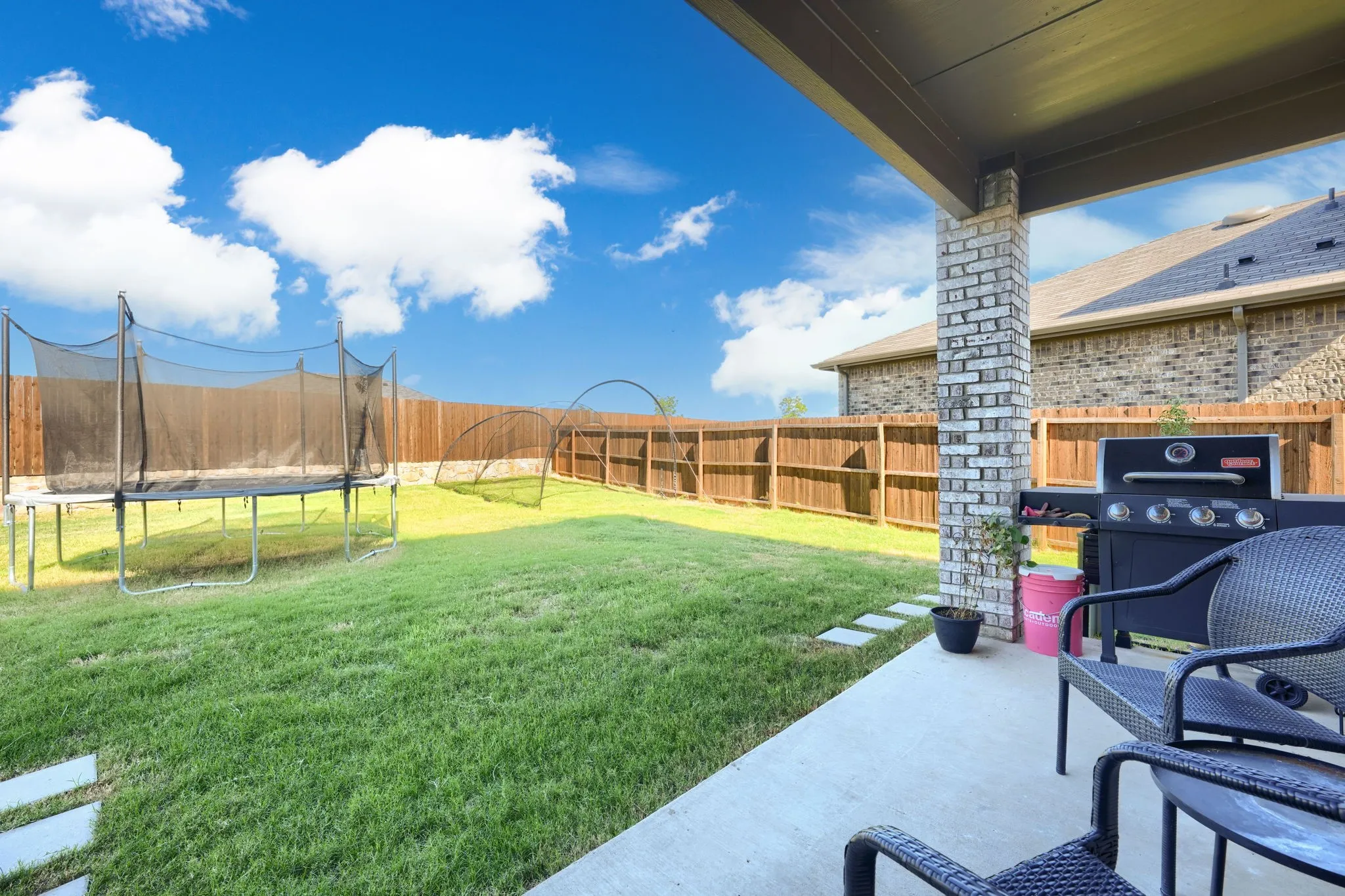 Expansive green space featuring a concrete patio, brick column, and wood privacy fence
