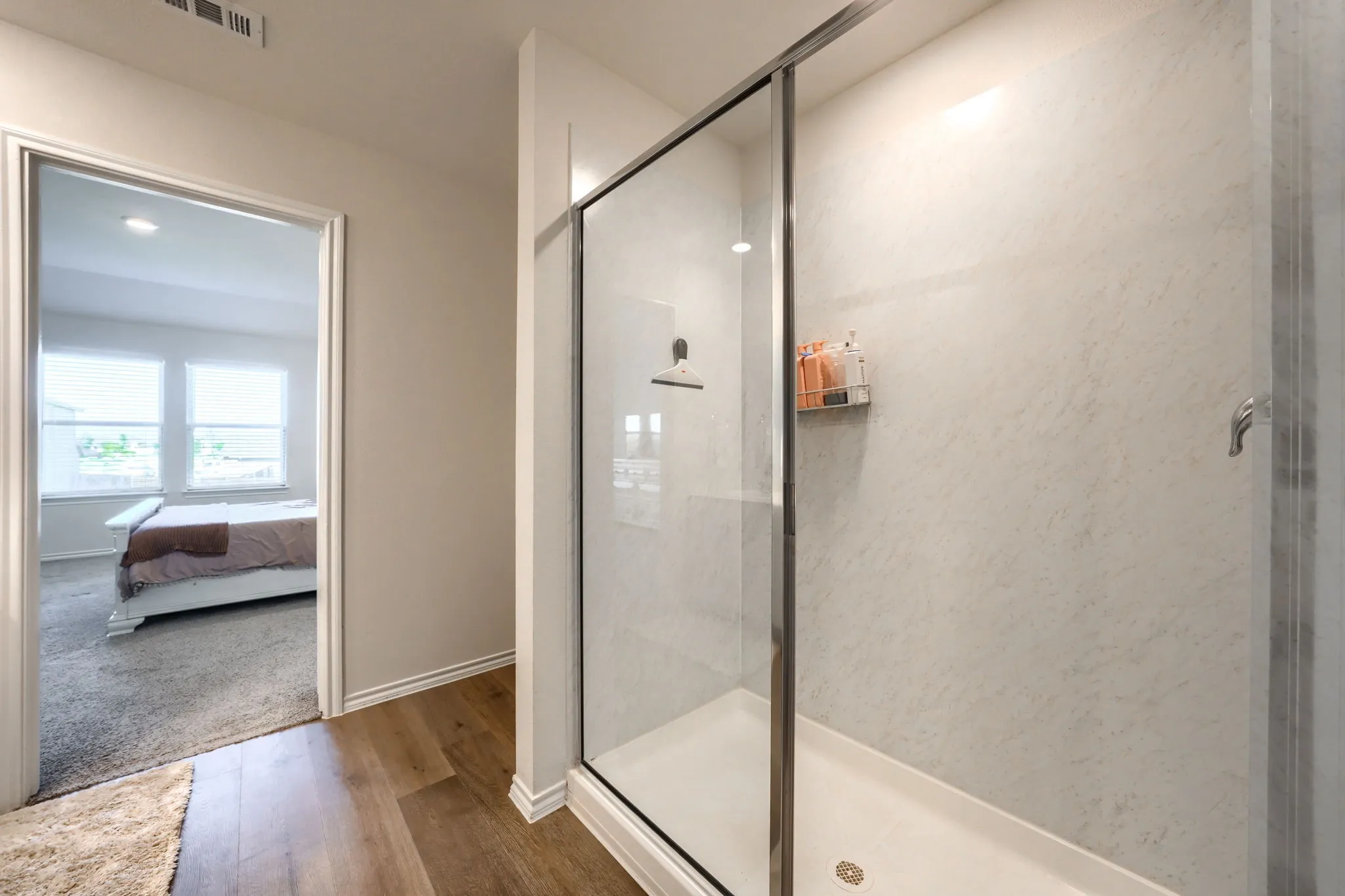 Glass-enclosed shower with a white shower base and light-toned wall panels