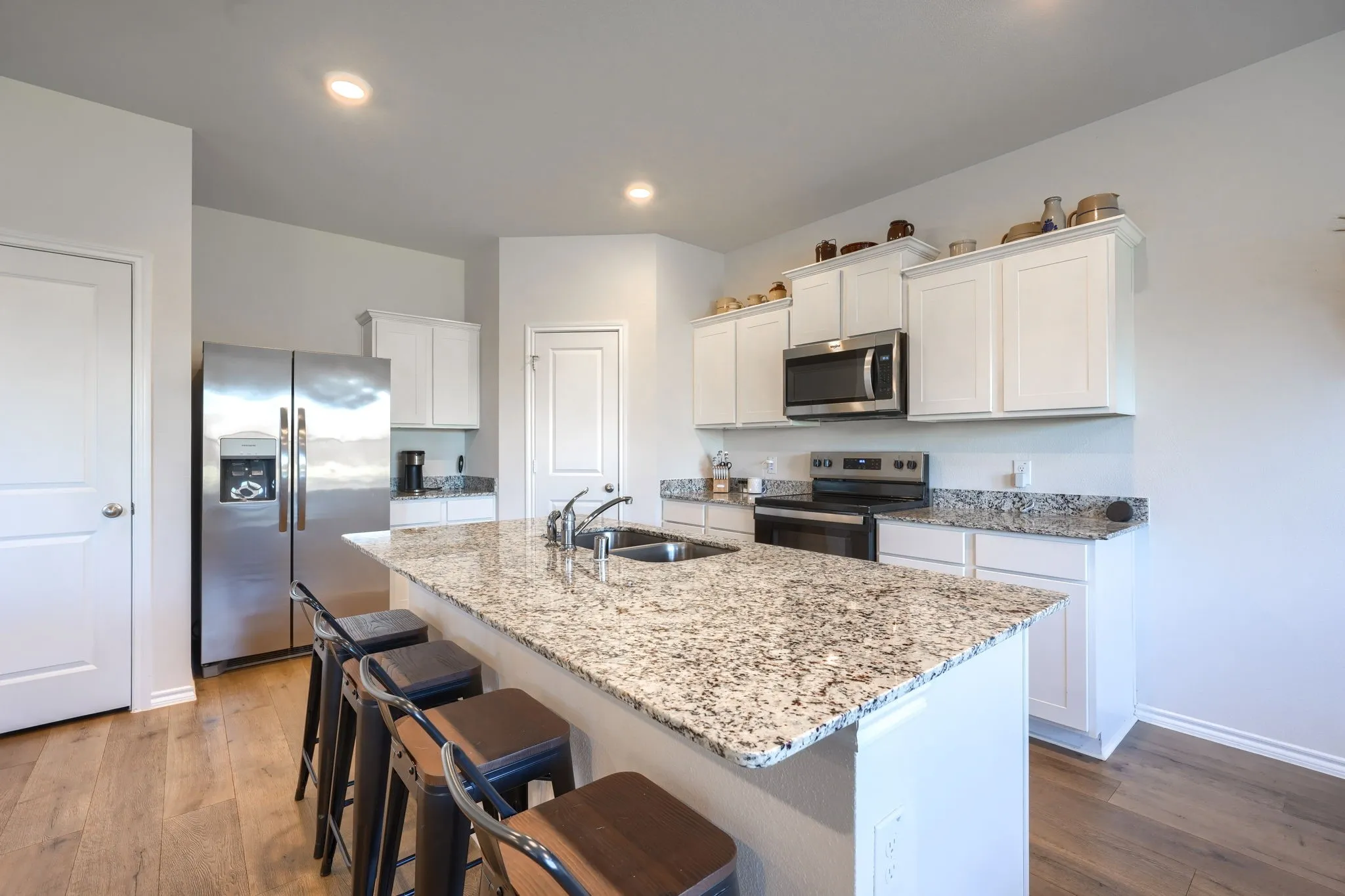 Kitchen featuring white cabinetry, stainless steel appliances, granite countertops, wood-finish flooring, and recessed lighting