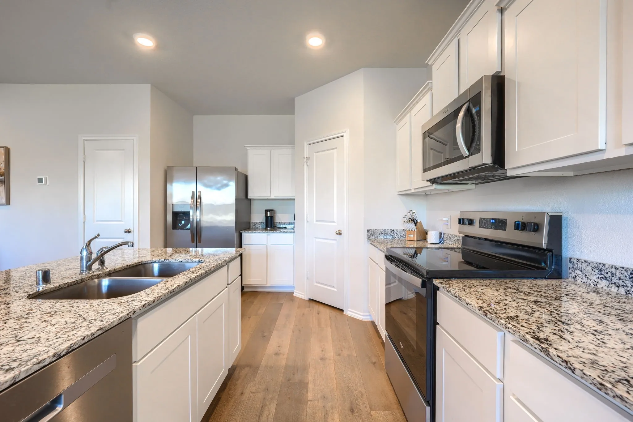 Kitchen featuring a double basin stainless steel sink, wood-finish flooring, white cabinetry, granite countertops, and stainless steel appliances