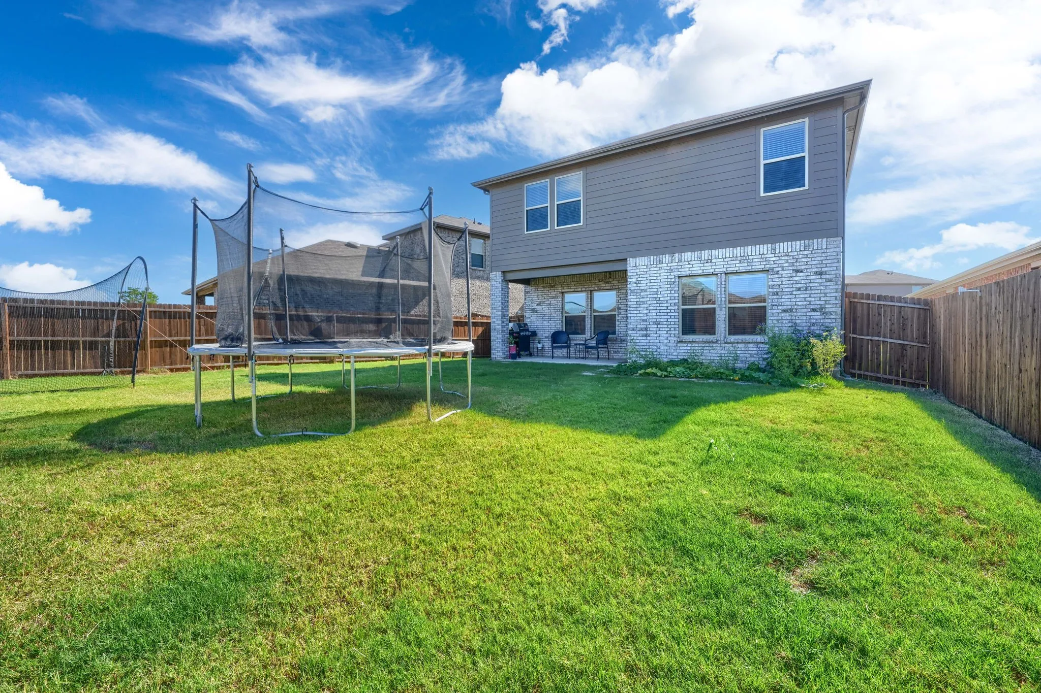Expansive backyard with a manicured lawn, full privacy fencing, and a lower-level patio