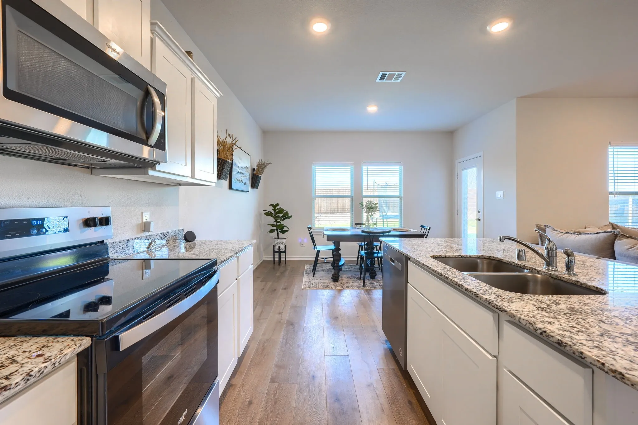 Kitchen featuring stainless steel appliances, white cabinetry, granite countertops, and wood-finish flooring