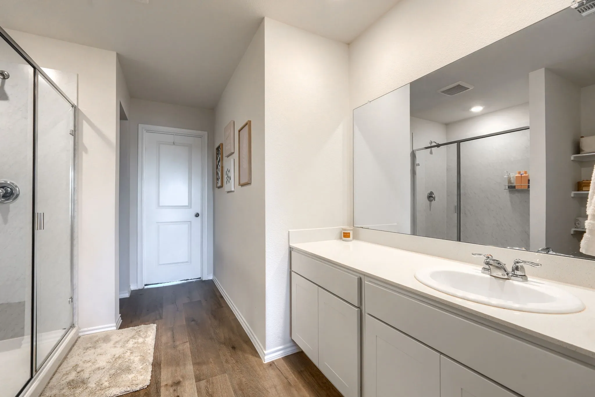 Integrated vanity with an undermount sink, expansive mirror, wood-finish flooring, and a glass-enclosed shower