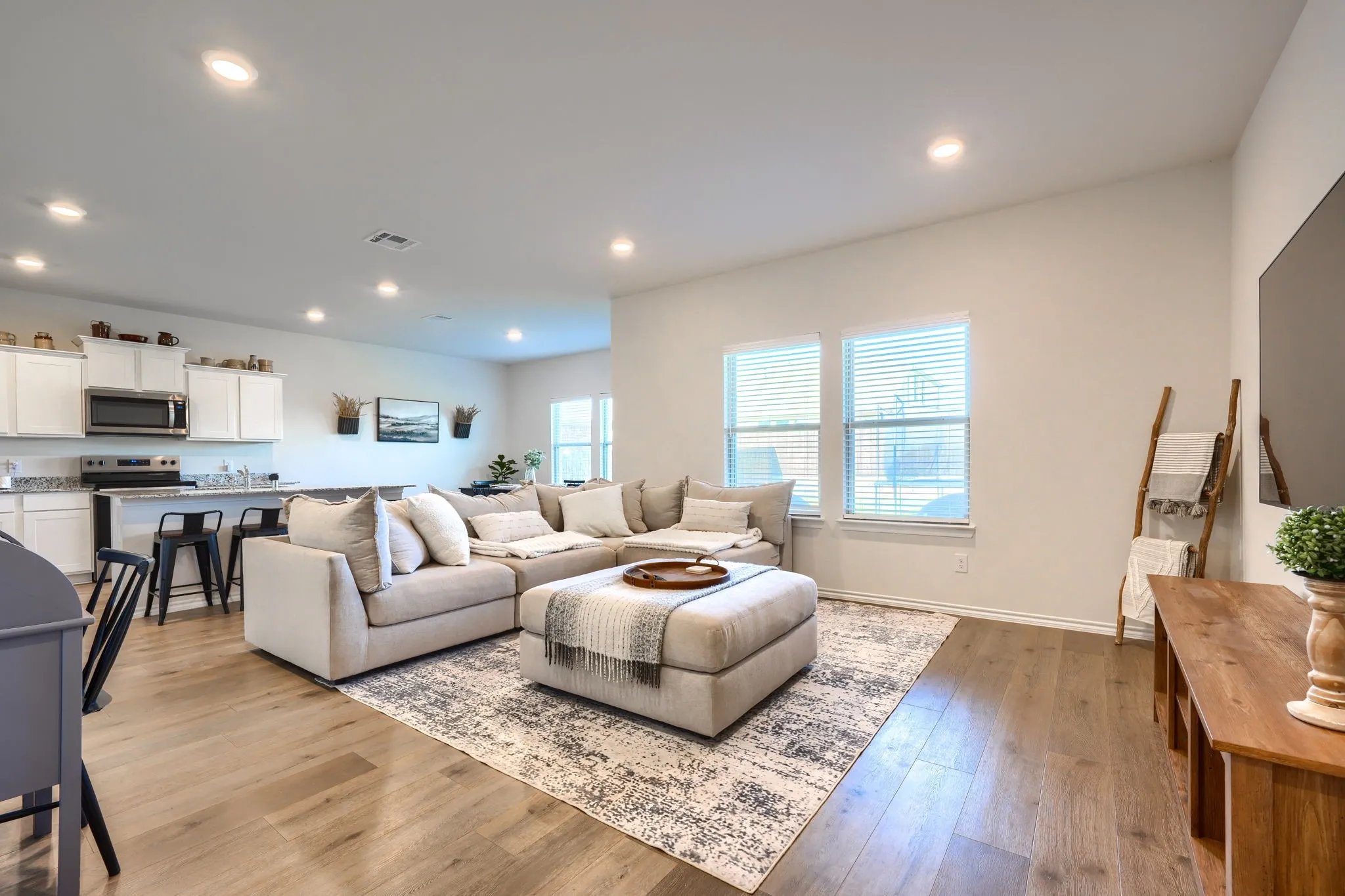 Open-concept living space with wood-finish flooring, recessed lighting, and kitchen with white cabinetry and granite countertops