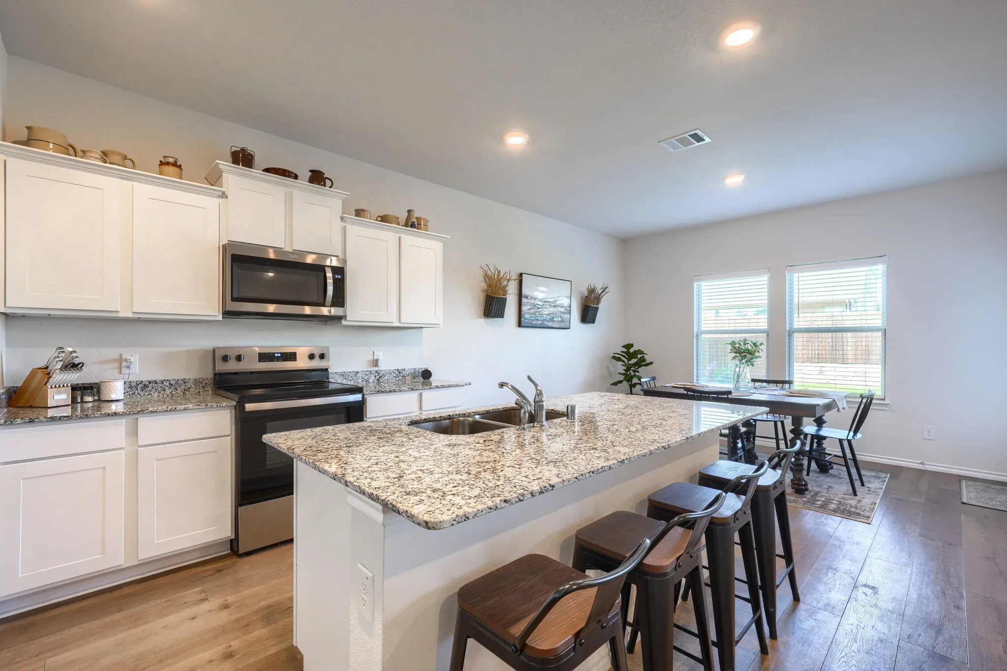 Kitchen featuring white cabinetry, granite countertops, stainless steel appliances, a kitchen island with seating, and wood-finish flooring