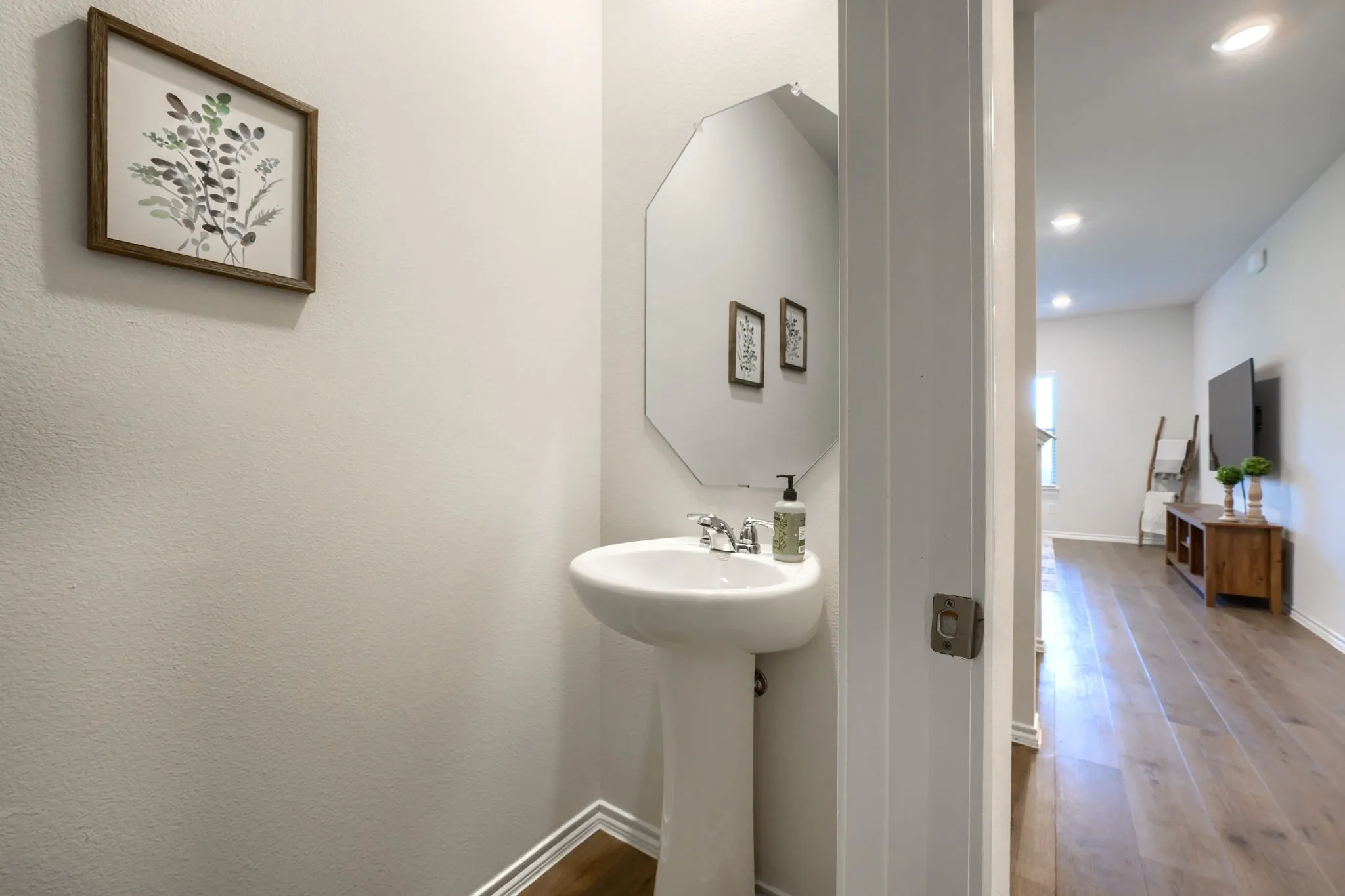 Pedestal sink with chrome-finish faucet, octagonal wall-mounted mirror, and wood-finish flooring