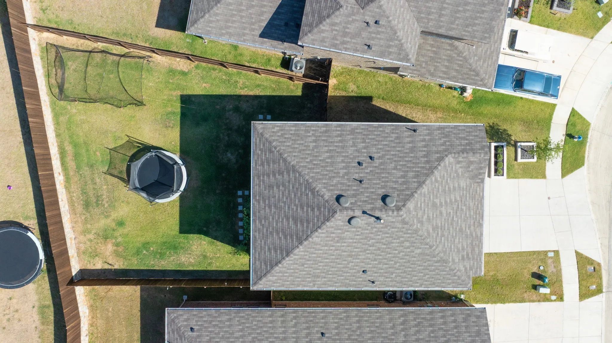 Manicured lawn with a wooden perimeter fence, stone paver pathway, and multiple rooflines featuring asphalt shingles