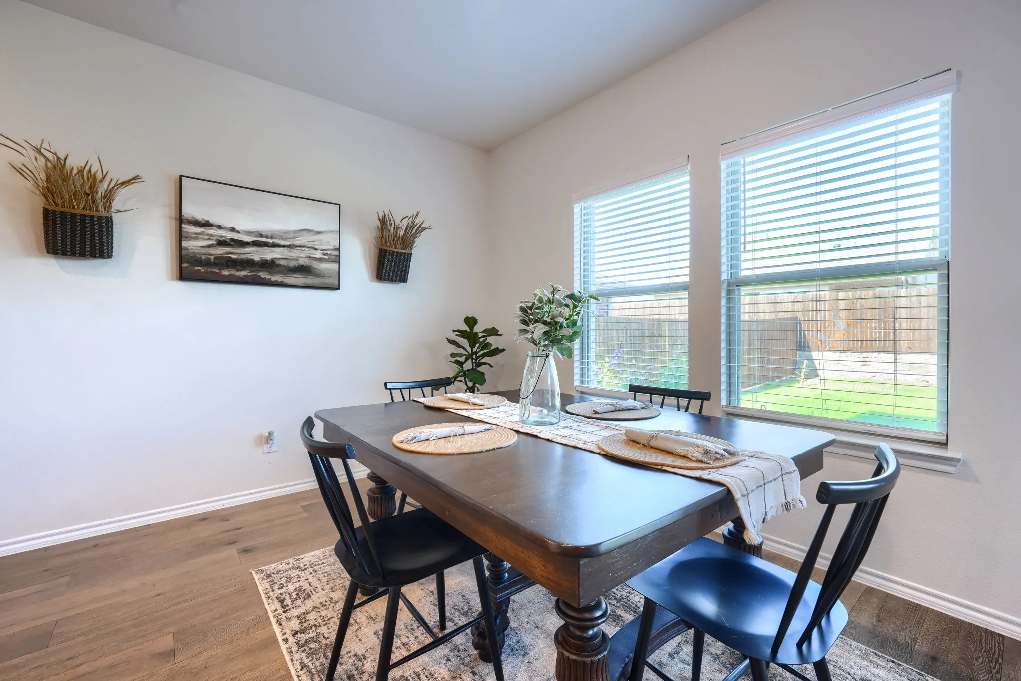 Wood-finish flooring with white trim, two windows with blinds, and white walls