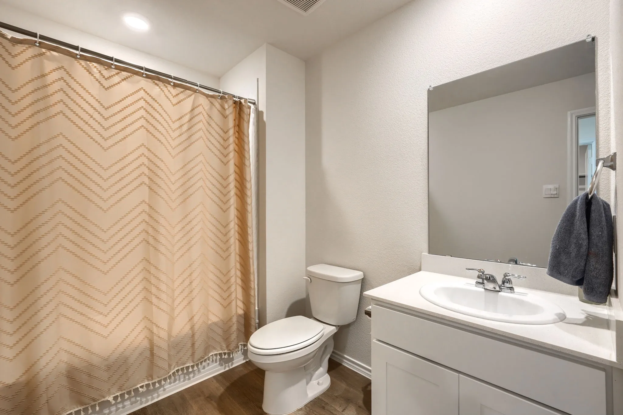 White vanity with a single basin sink, chrome faucet, wall-mounted mirror, and wood-finish flooring