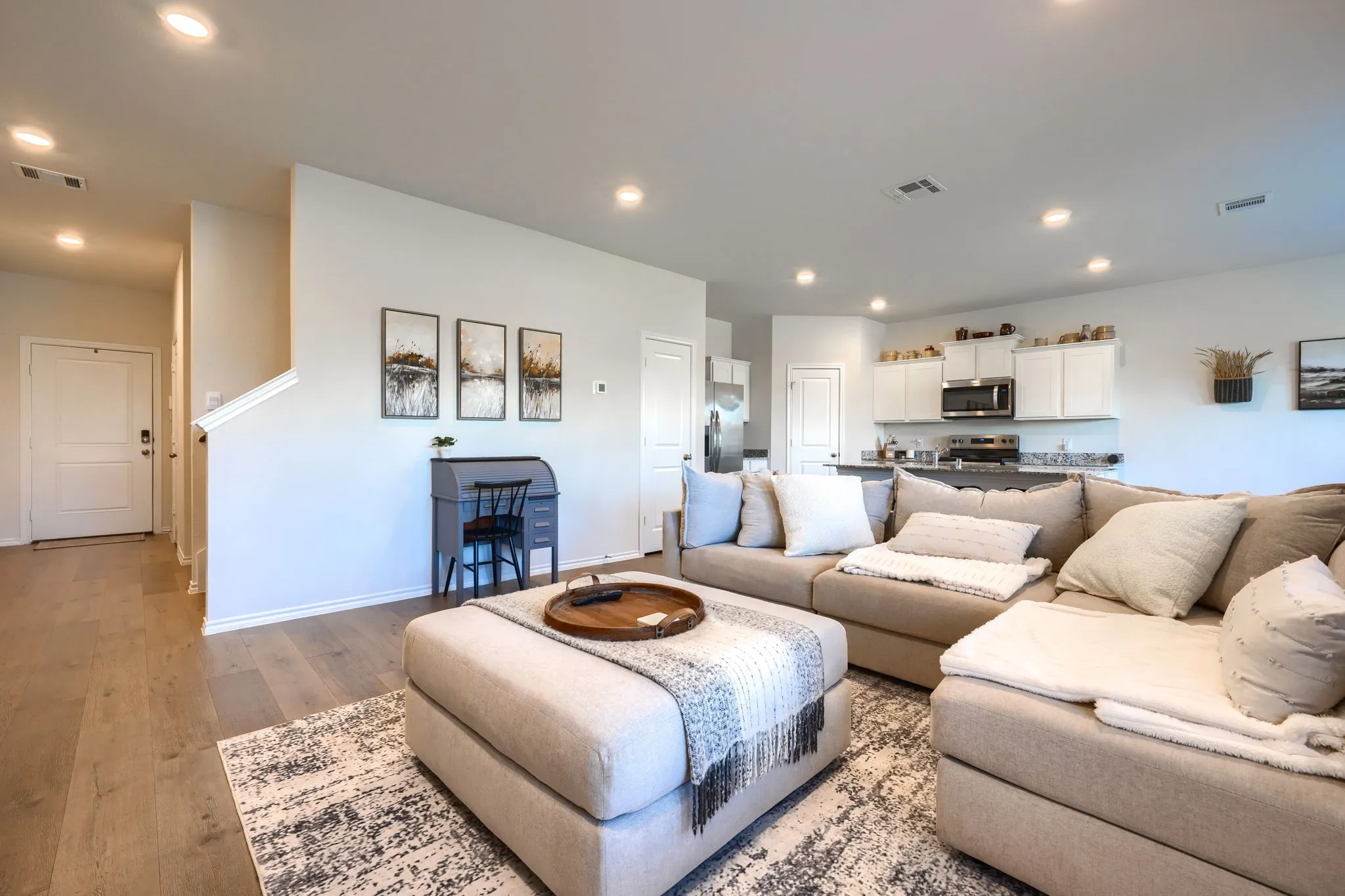 Open-concept living space featuring recessed lighting, wood-finish flooring, white walls, and a kitchen with white cabinetry and stainless steel appliances