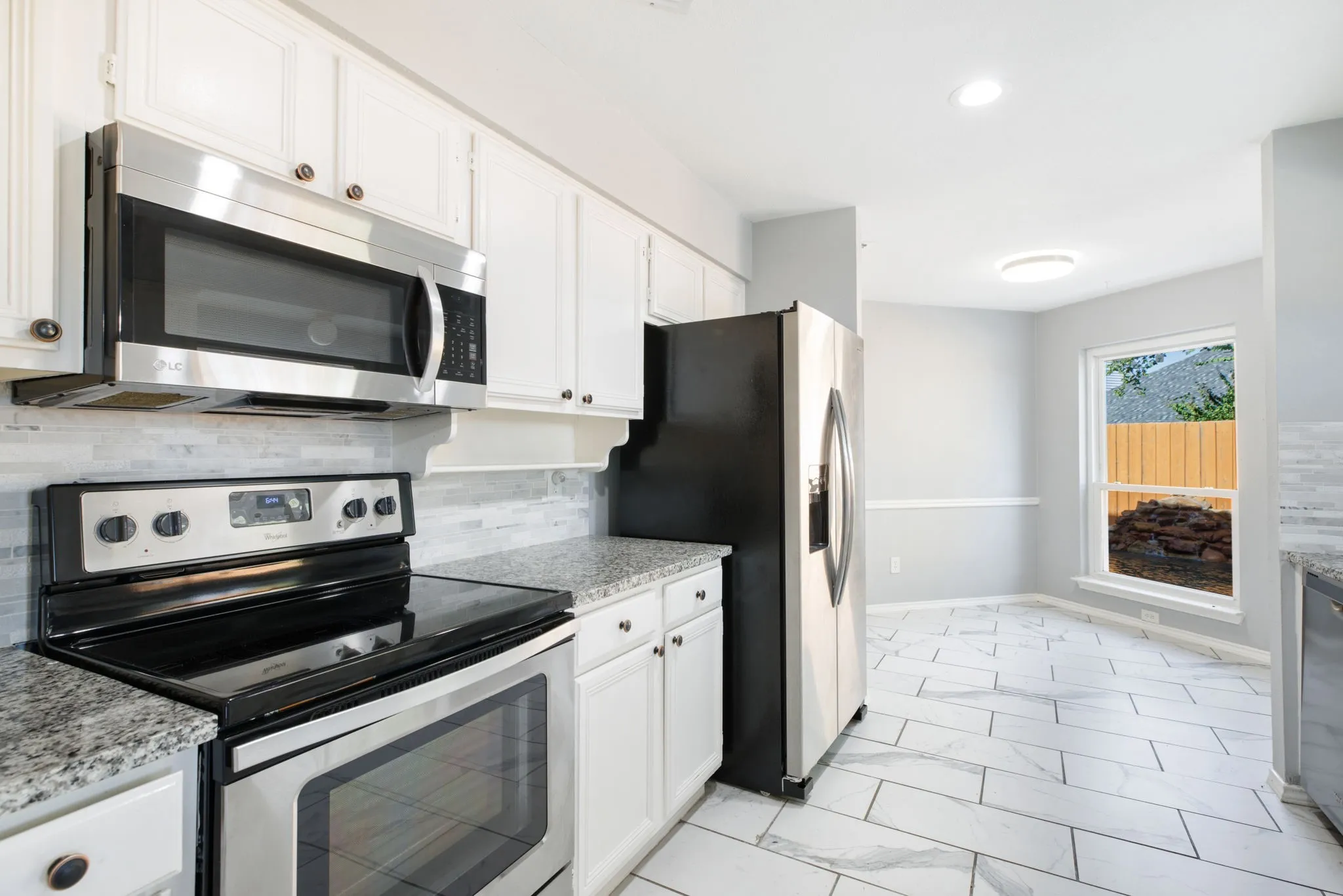 White cabinetry with dark hardware, stainless steel appliances, speckled countertops, tile backsplash, and light-toned tile flooring