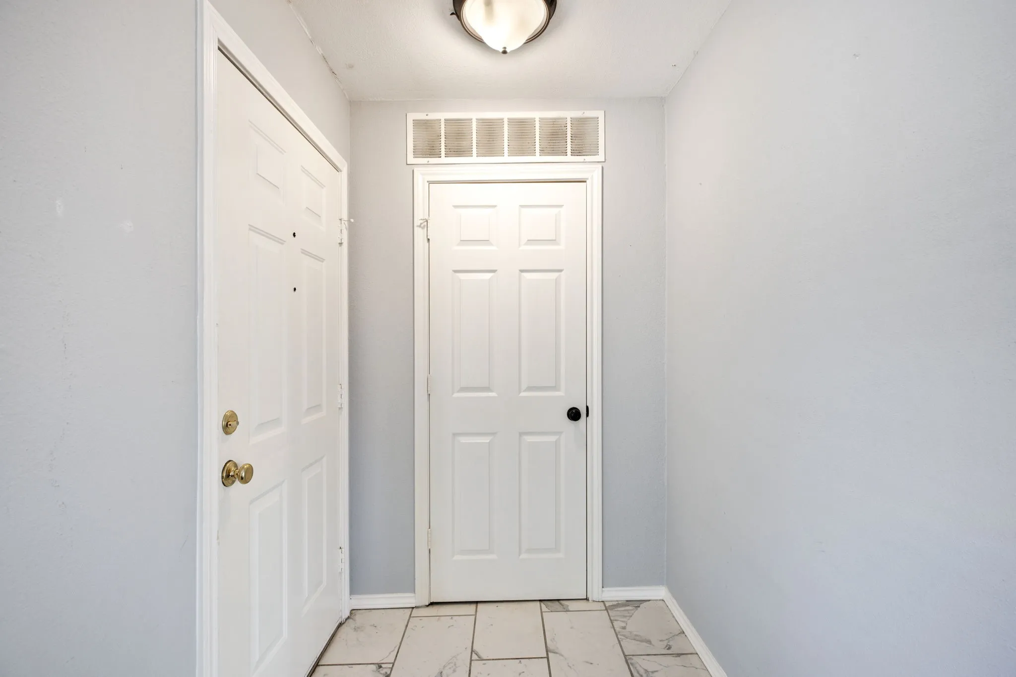 Recessed entry with light gray walls, ceiling-mounted light fixture, and tile flooring