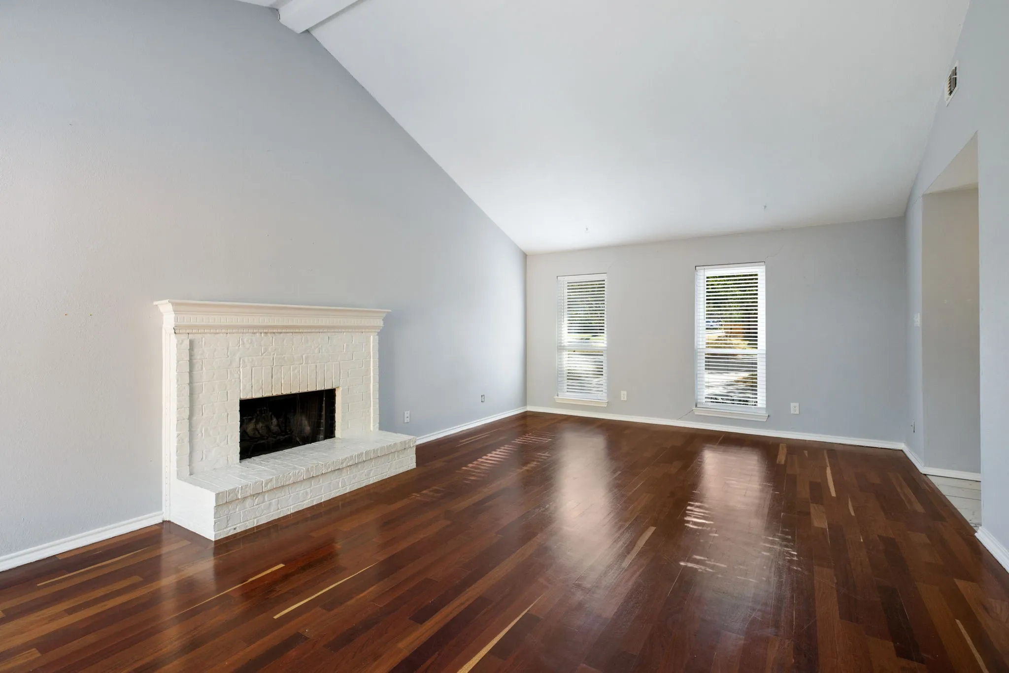 Spacious room featuring rich wood-finish flooring, a white brick fireplace with a detailed mantel, and high vaulted ceilings