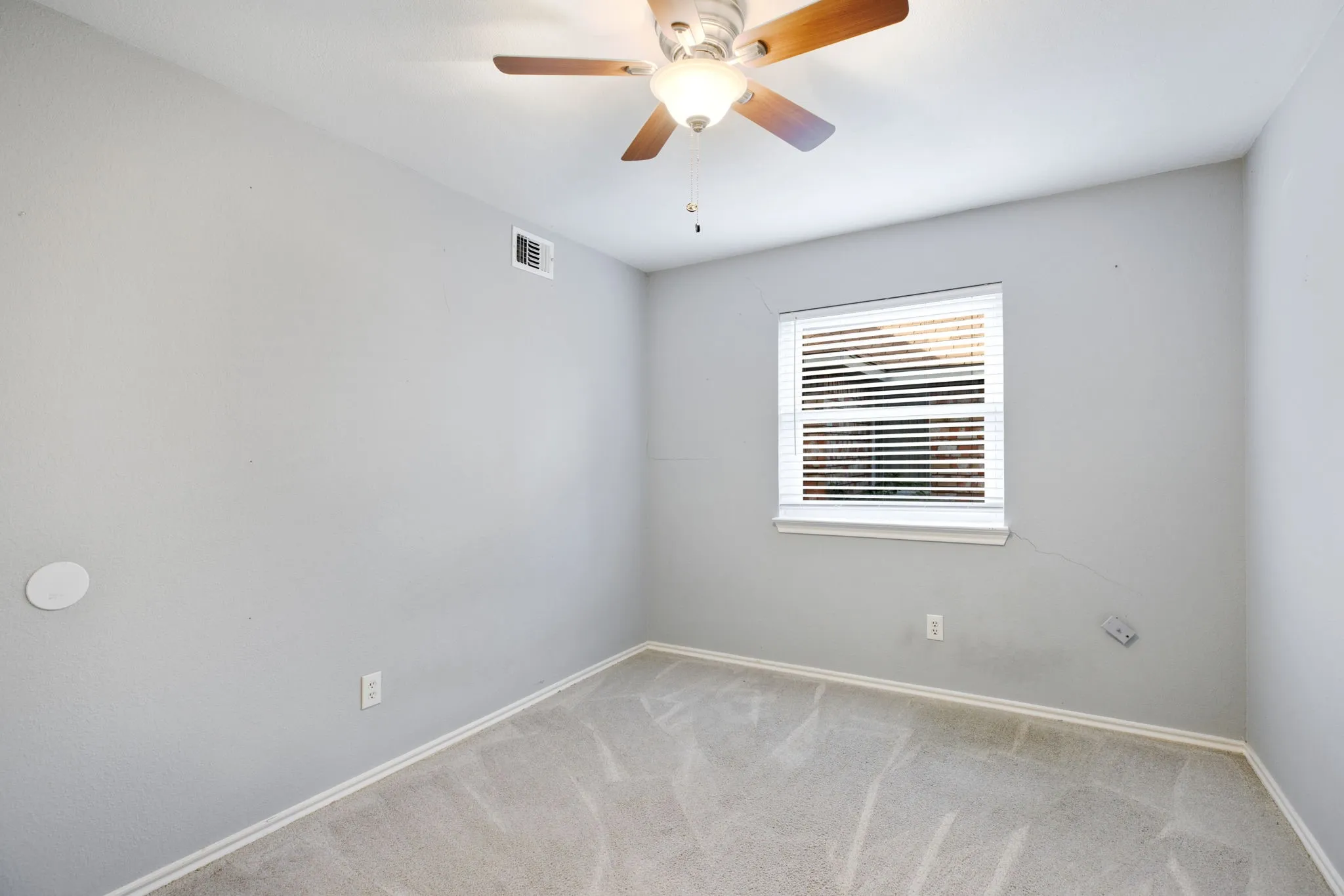Textured walls, ceiling fan with light fixture, window with blinds, carpeted flooring, and wall-mounted electrical outlets