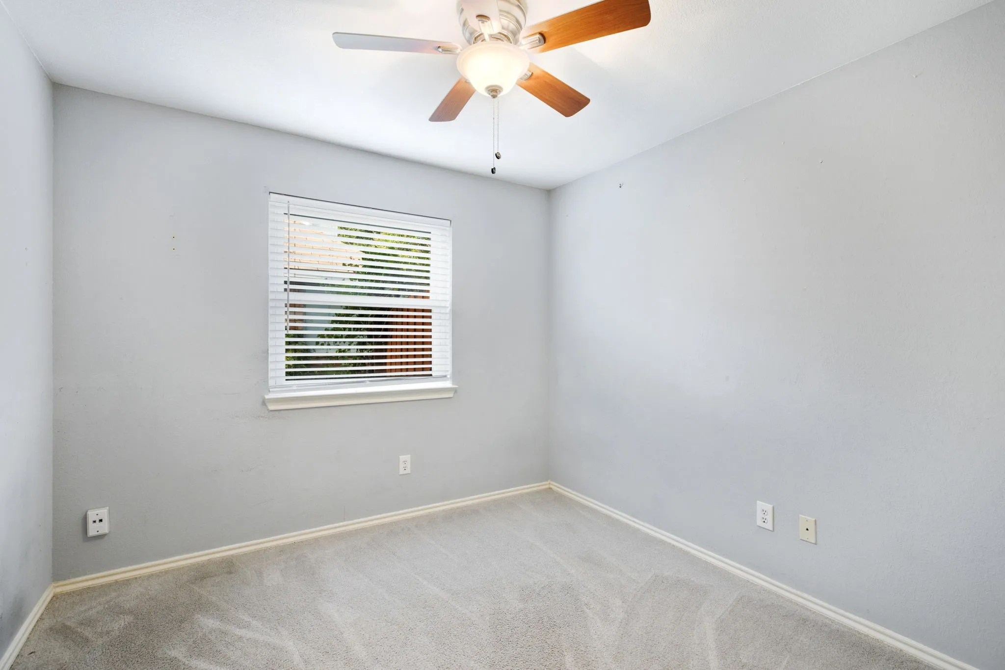 Neutral gray walls, light gray carpeting, ceiling fan with light fixture, and a window with blinds