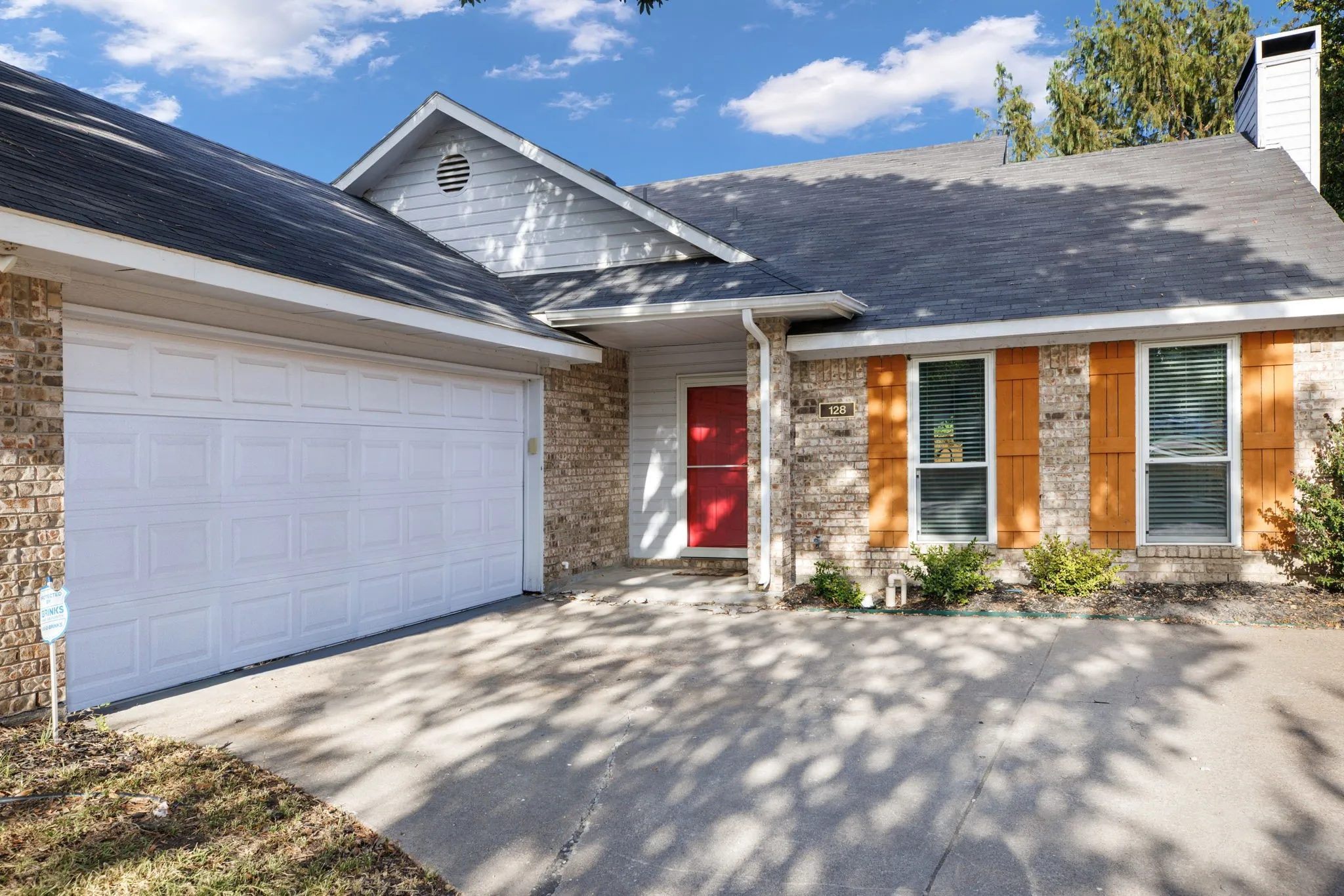 Brick and siding exterior with a shingle roof, featuring a red entry door, decorative wood shutters, and an attached garage with a concrete driveway