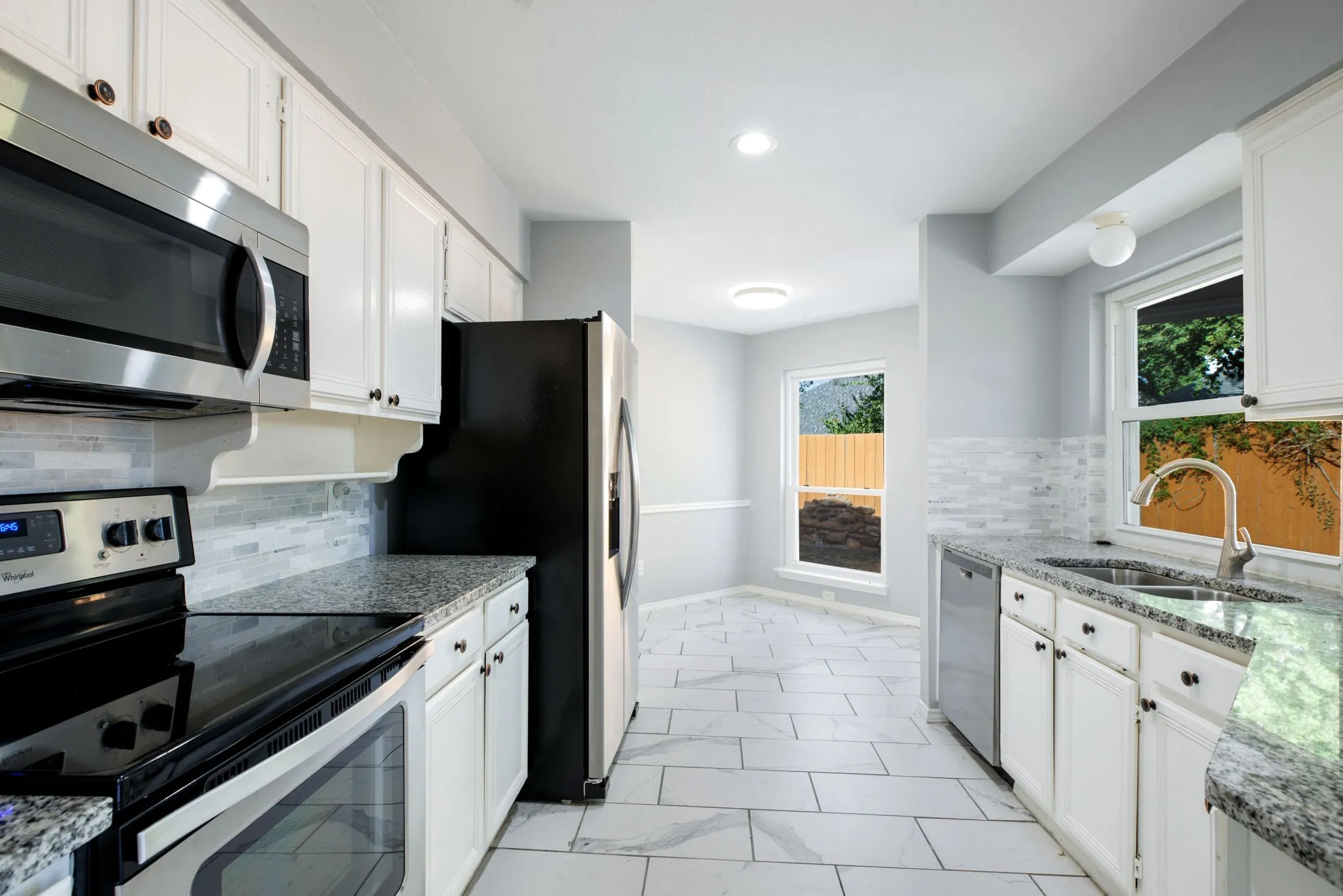 Well-appointed kitchen featuring white cabinetry, stainless steel appliances, granite countertops, a tiled backsplash, and light-toned tile flooring
