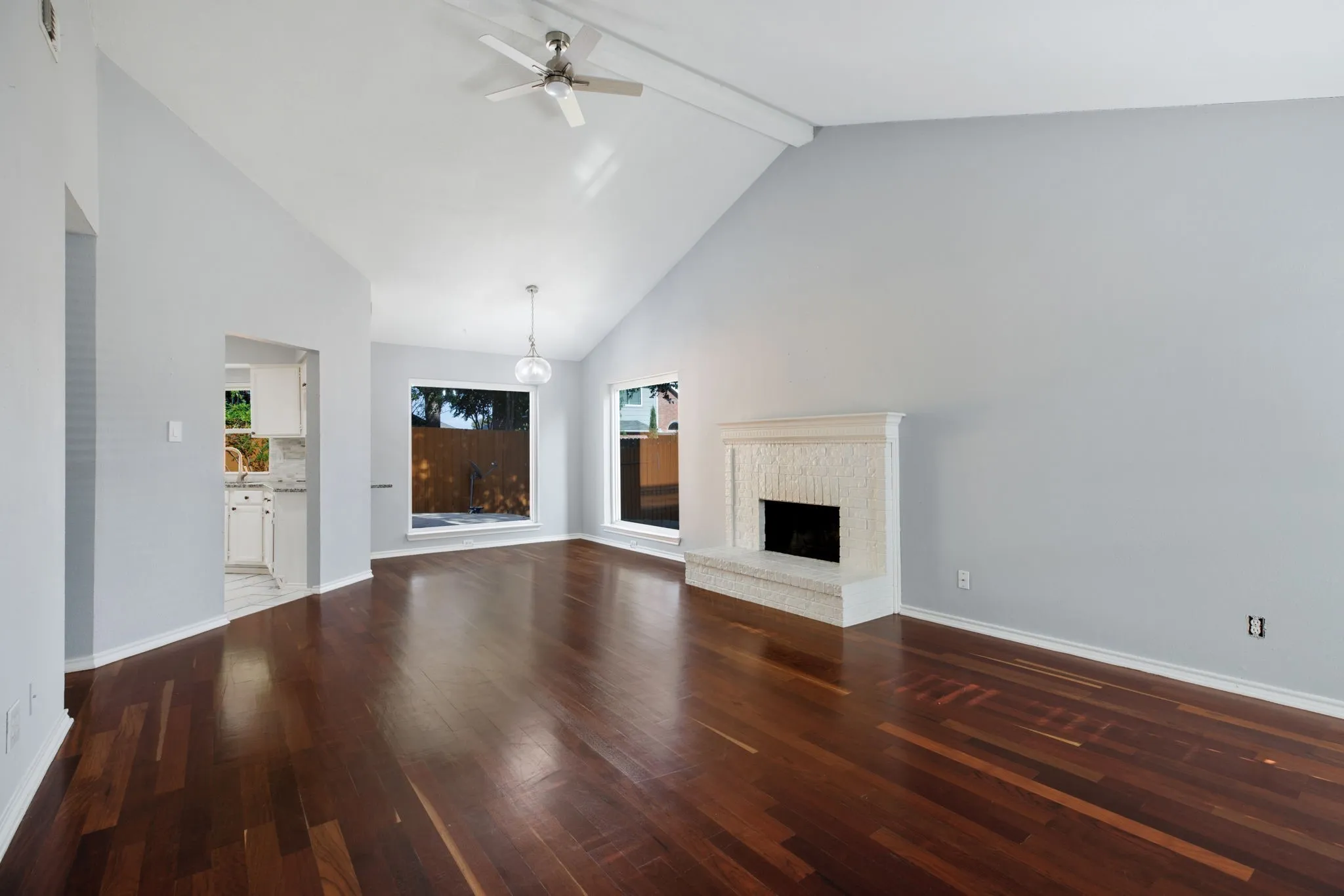 Vaulted ceiling with a ceiling fan, wood-finish flooring, white brick fireplace, and large windows