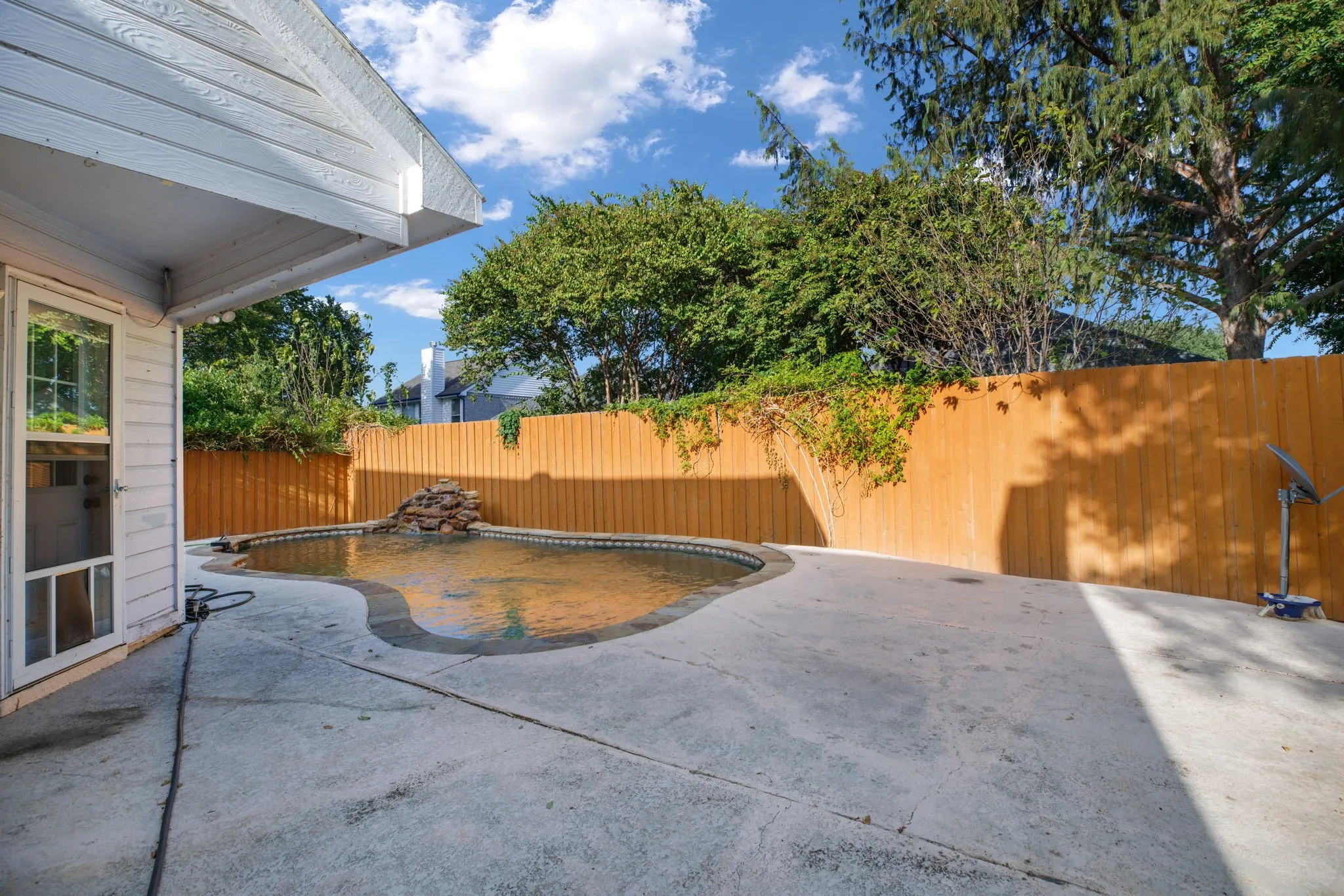 Outdoor concrete patio with a built-in pool, rock water feature, and wood privacy fencing
