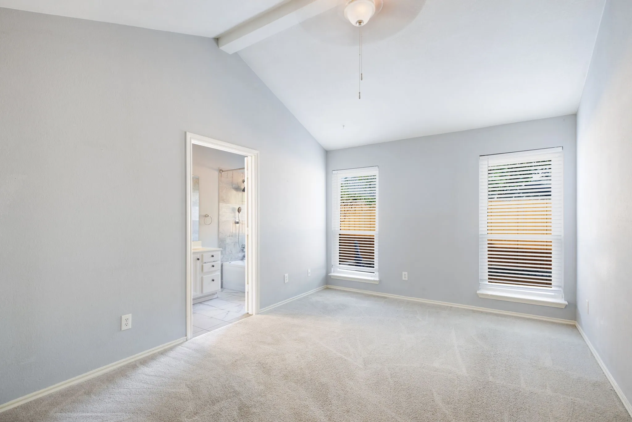 Vaulted ceiling with an exposed beam and ceiling fan, two windows with blinds, and light-toned carpeting