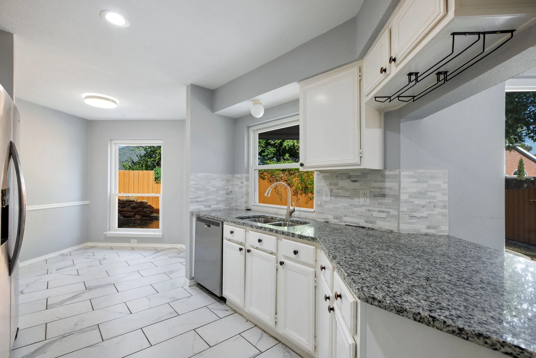 Contemporary kitchen featuring white cabinetry, stone-finish countertops, stainless-steel dishwasher, and a mosaic tile backsplash