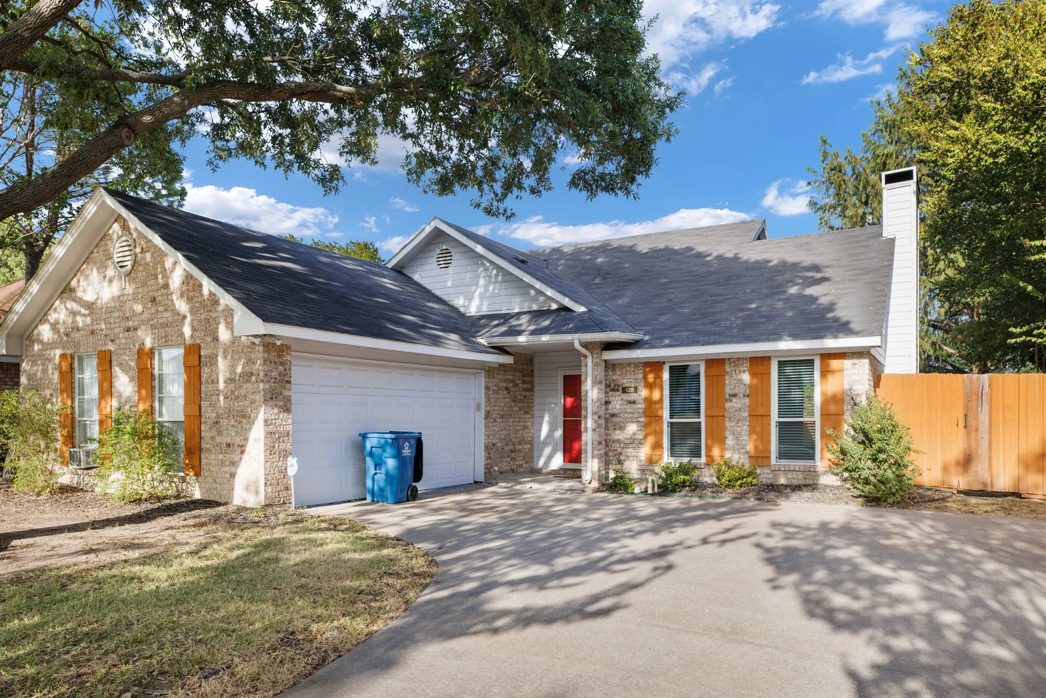 Brick facade with contrasting wood-finish window shutters, attached garage, and a red entry door