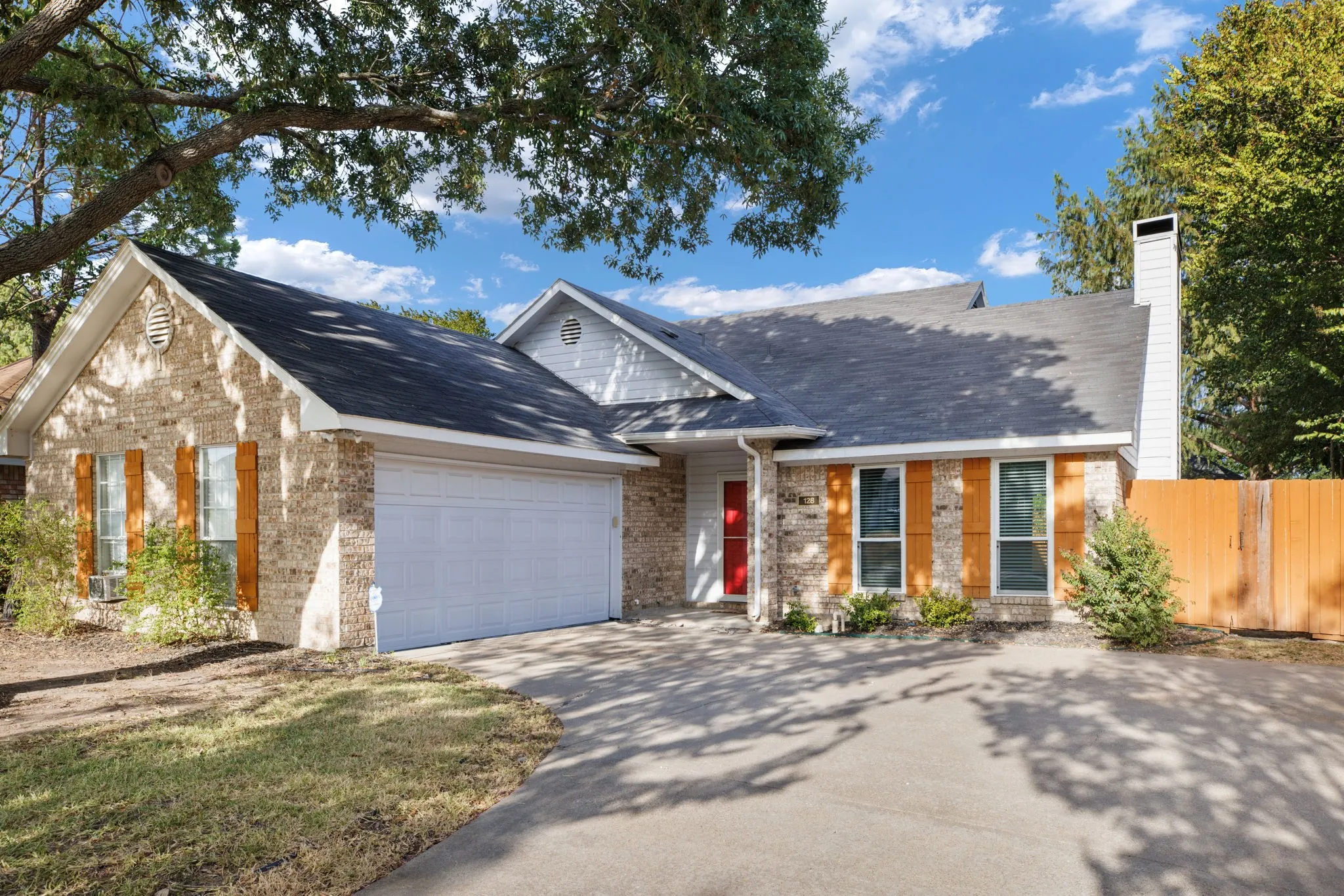 Brick exterior with wood shutters, attached two-car garage, and a red entry door