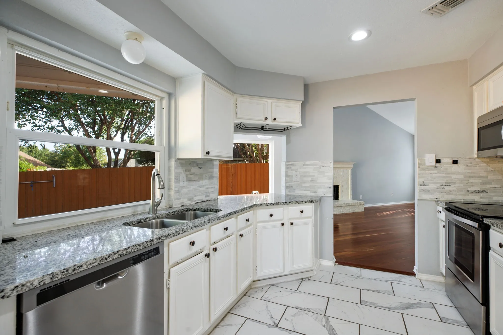White cabinetry, stainless steel appliances, dual basin sink, light-toned backsplash, and patterned floor tiling
