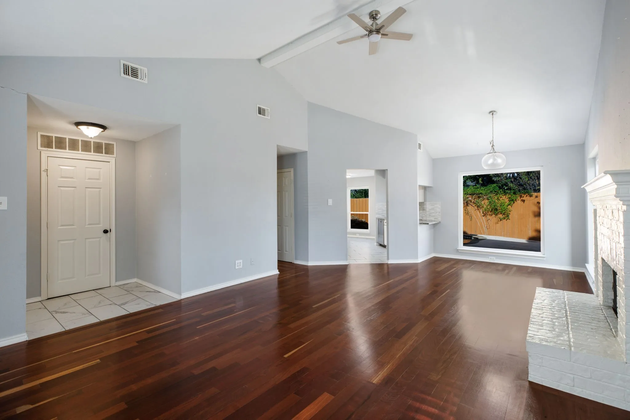 Vaulted ceilings, wood-finish flooring, white brick fireplace, ceiling fan, and decorative pendant light fixture