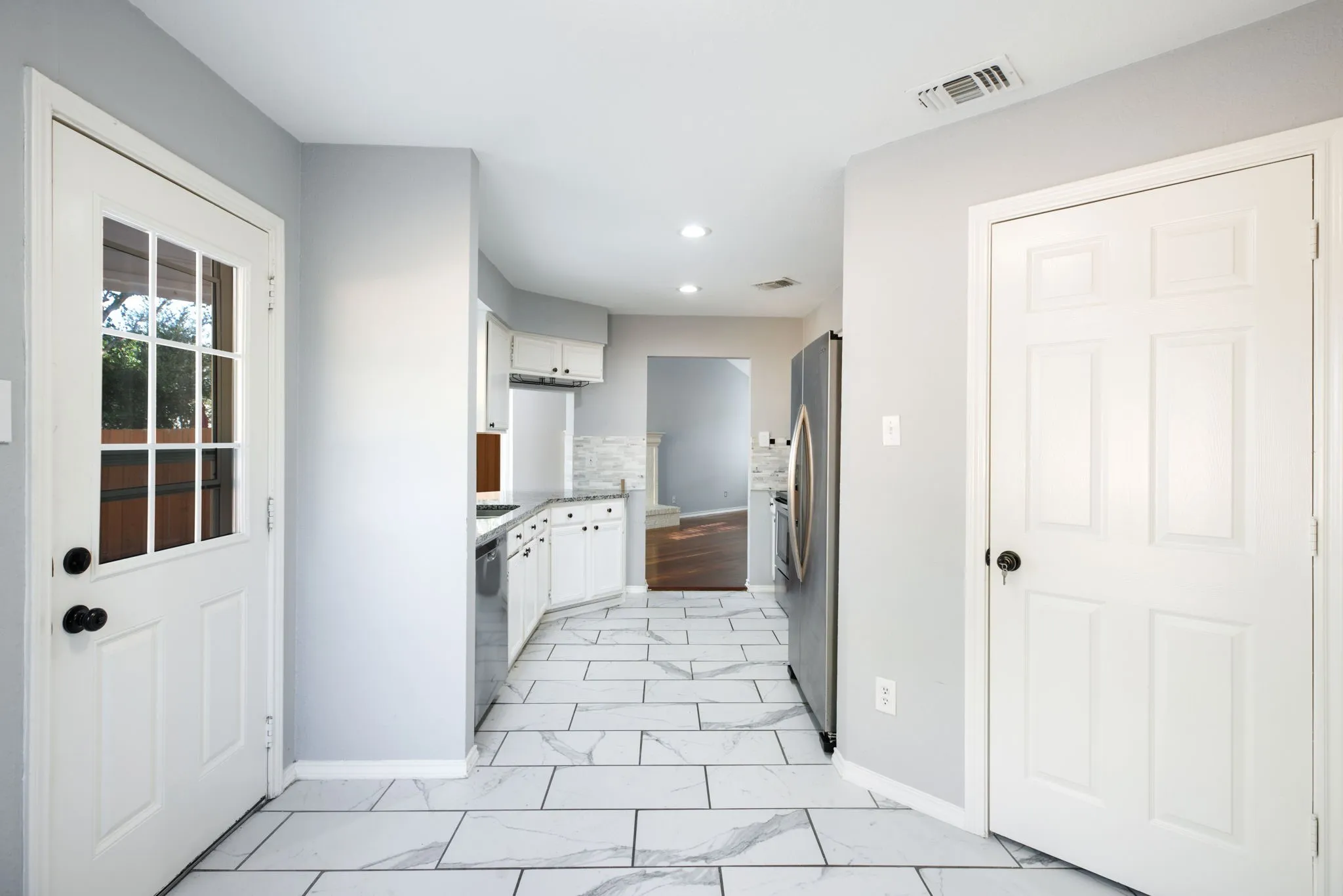 Kitchen featuring white cabinetry, stainless steel refrigerator, light-toned backsplash, white paneled doors, and large format rectangular floor tiles